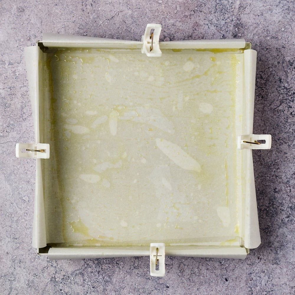 An 8 x 8-inch cake pan lined with parchment paper, which is clipped to each edge of the pan.