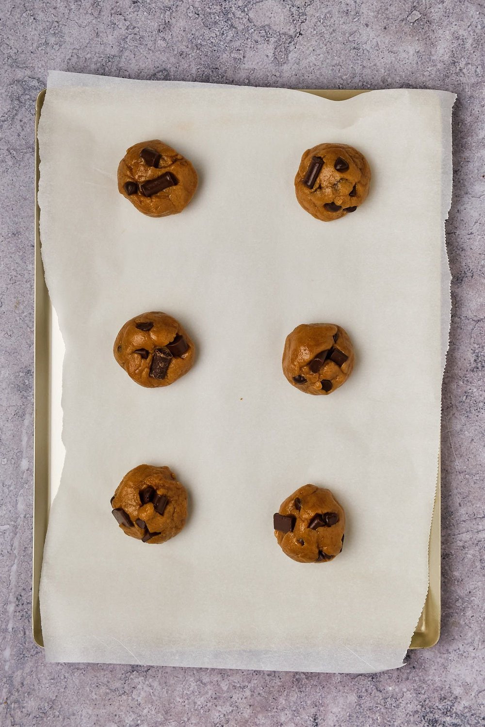 Balls of vegan chocolate chip cookie dough on a parchment-lined baking tray.