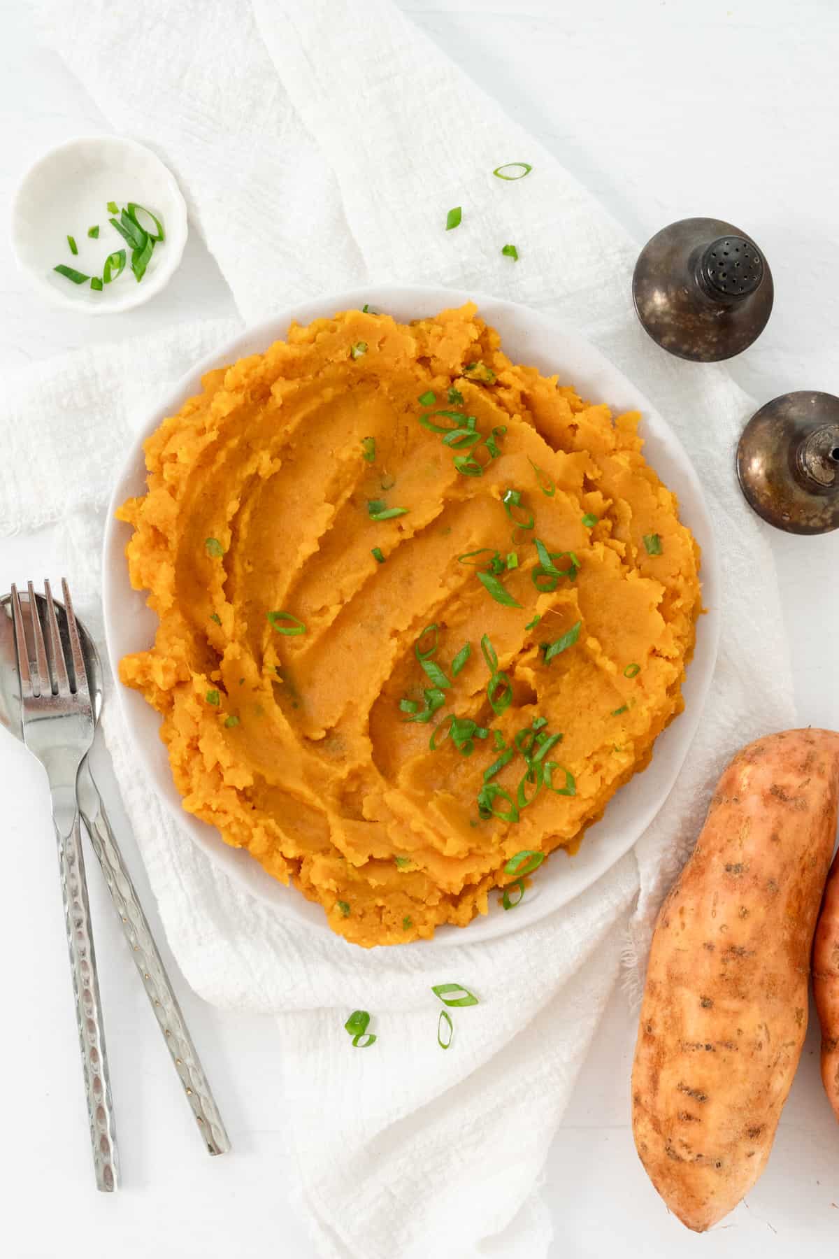 Vegan sweet potato mash on a plate topped with chopped green onions.