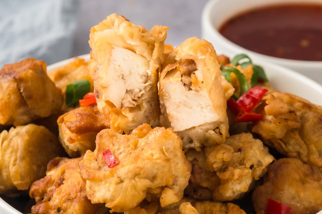 A bowl of crispy fried tofu, with the top piece cut open to show the inside texture.