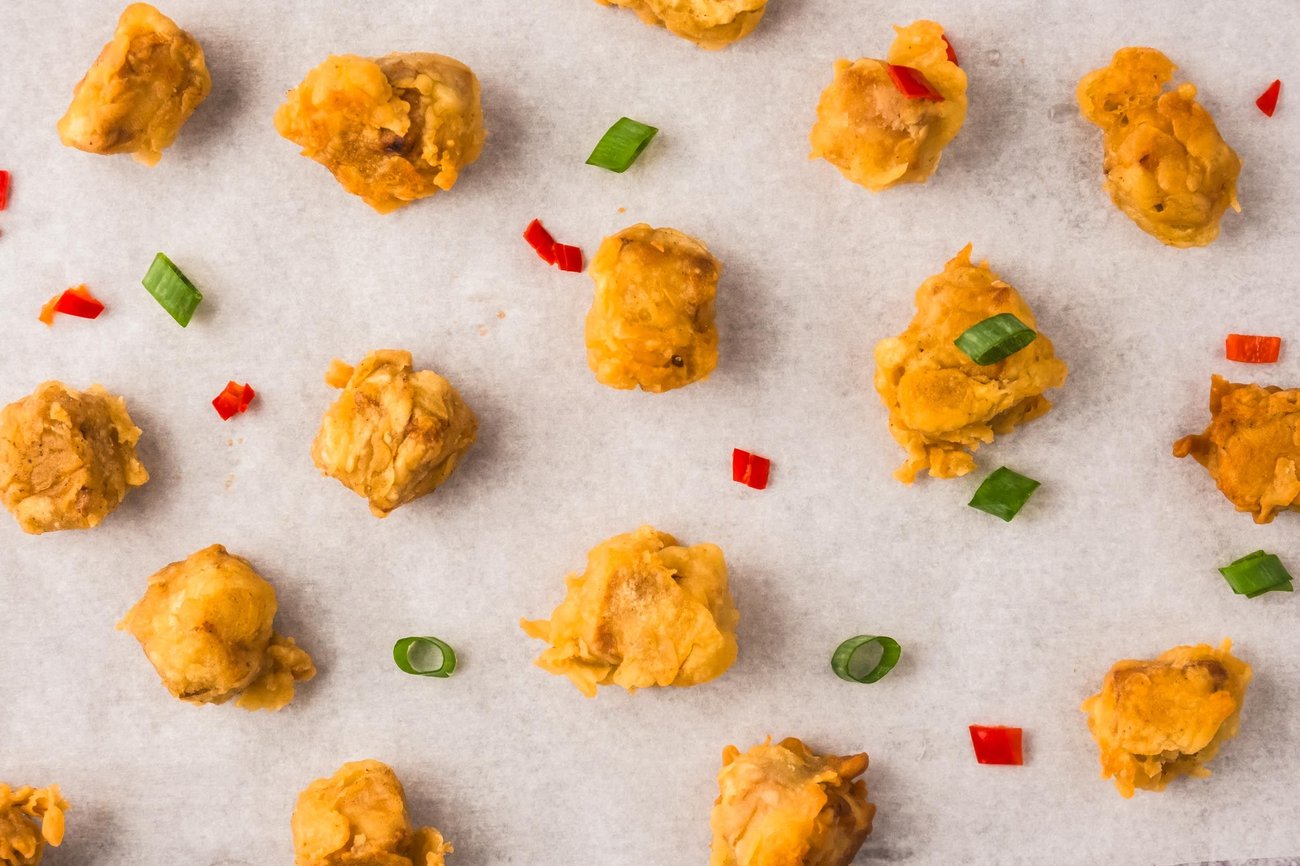 Pieces of crispy tofu on parchment paper with small pieces of green onion and red pepper.