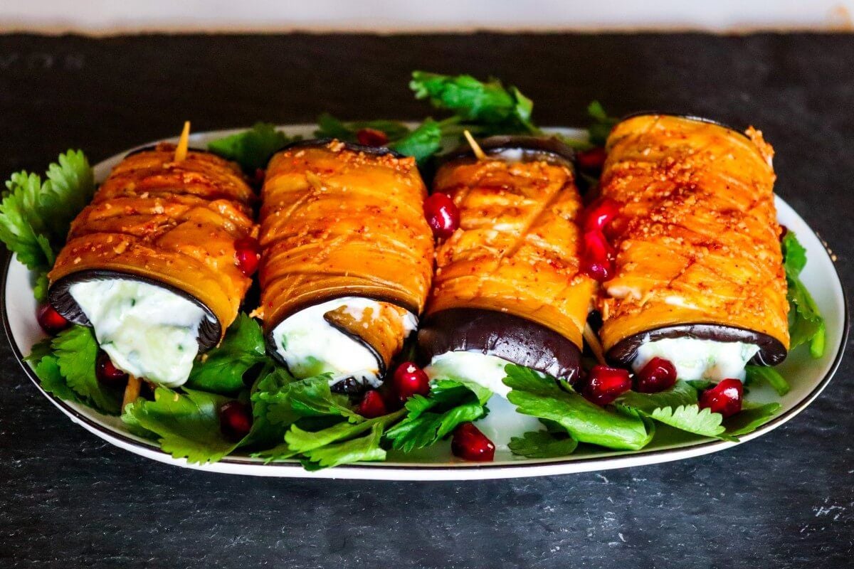 Four vegan eggplant rollups on a serving platter on a bed of greens. 