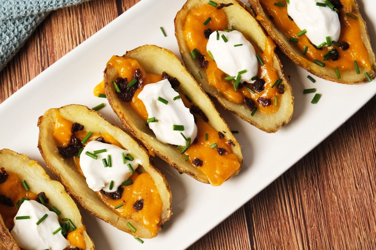 A top-down view of vegan potato skins on a platter with vegan cheddar, sun-dried tomatoes, vegan sour cream, and chives.