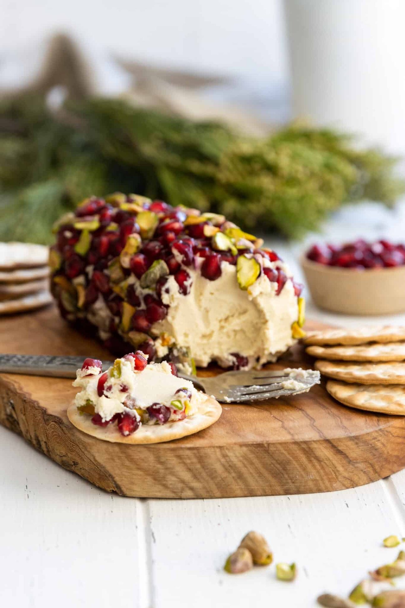 Vegan cheese log with pomegranate and pistachios on a platter with crackers. 