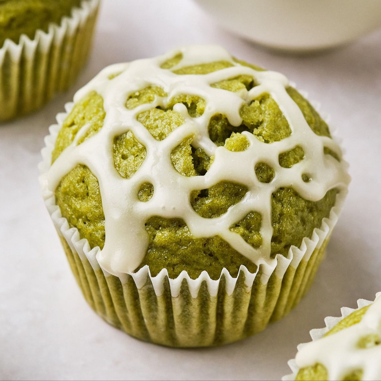A close-up view of a vegan matcha muffin, topped with a vanilla icing drizzle. 