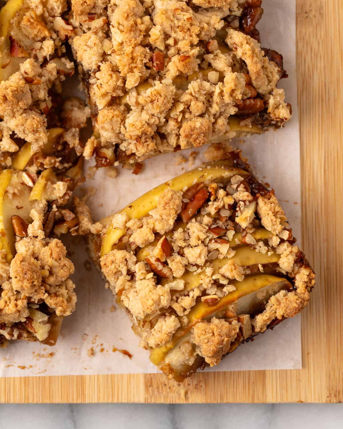 Cut apple crisp bars on a parchment-lined cutting board.