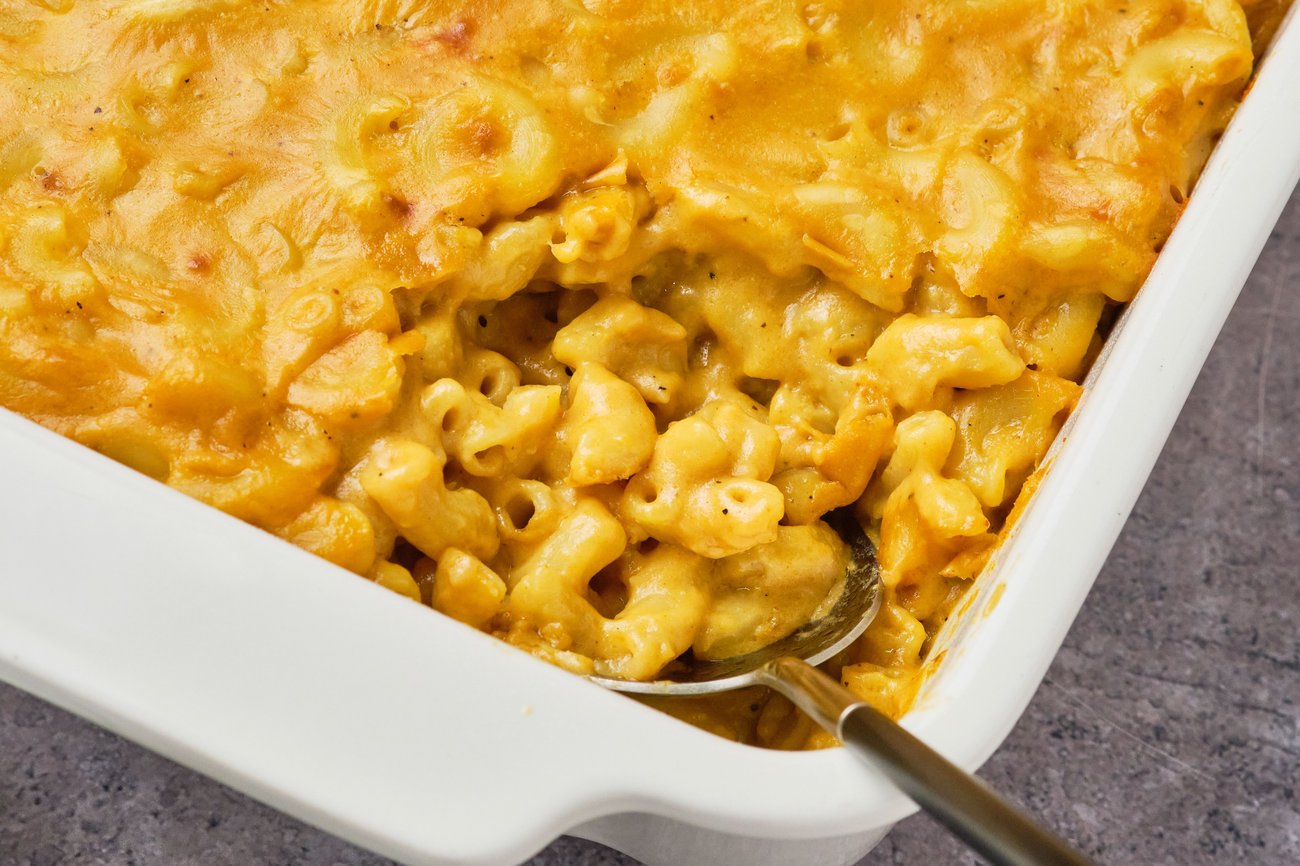 A close-up view of vegan mac and cheese in a casserole dish with a serving spoon.