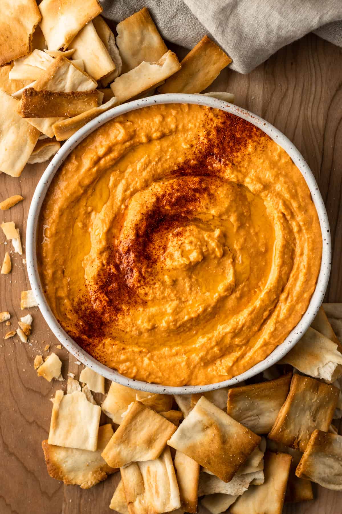 White bean buffalo hummus in a bowl on a table, surrounded by pita chips. 
