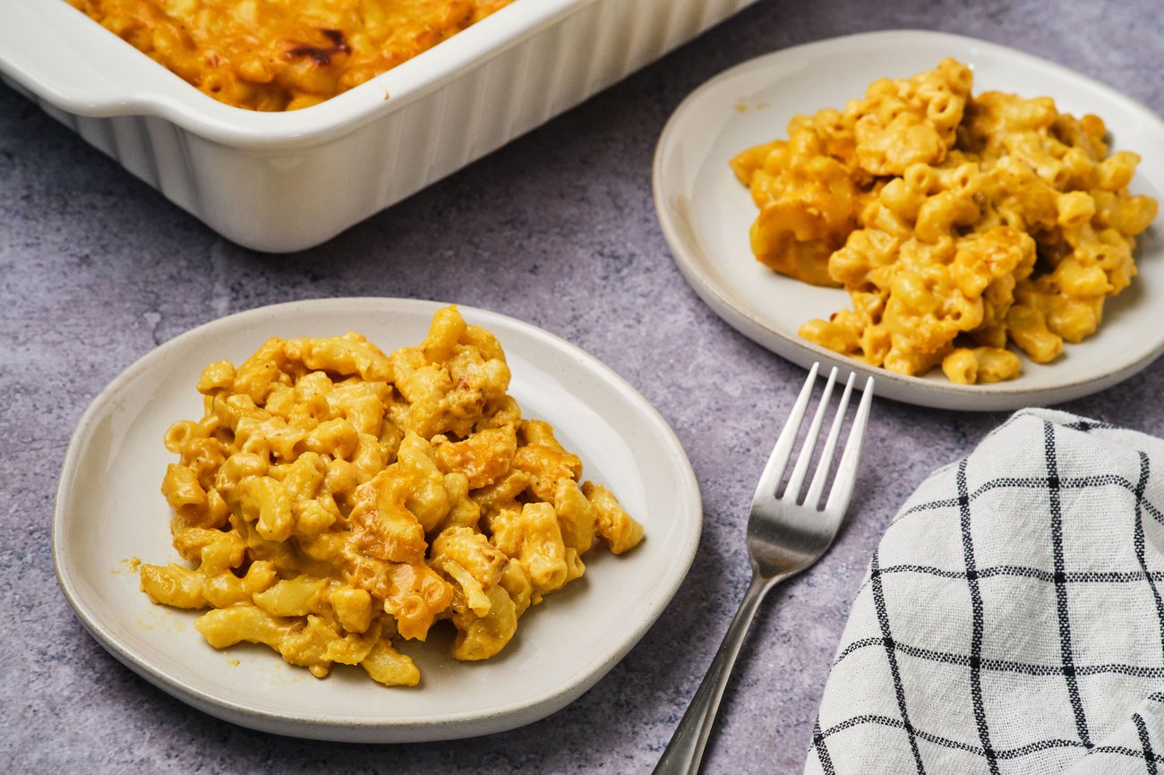Vegan mac and cheese on 2 plates with a casserole dish in the background; a fork and linen are also on the table.