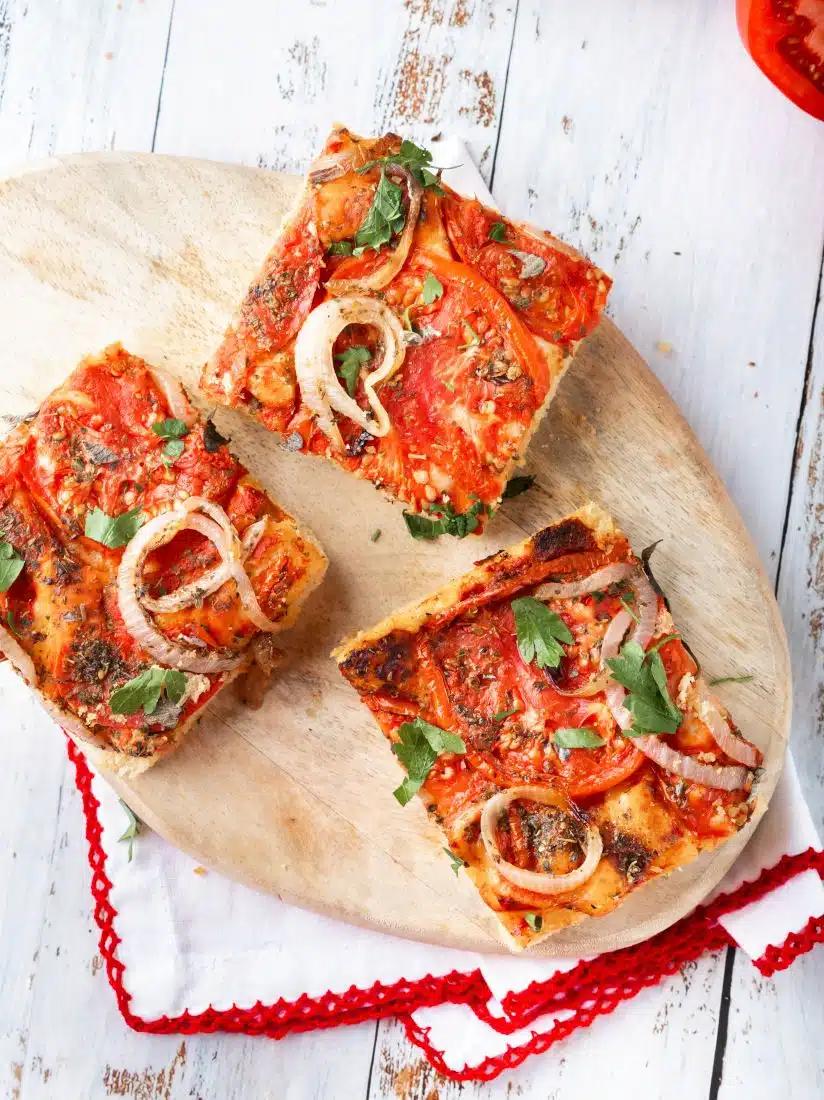 Three slices of ladenia on a wooden platter with a linen underneath.