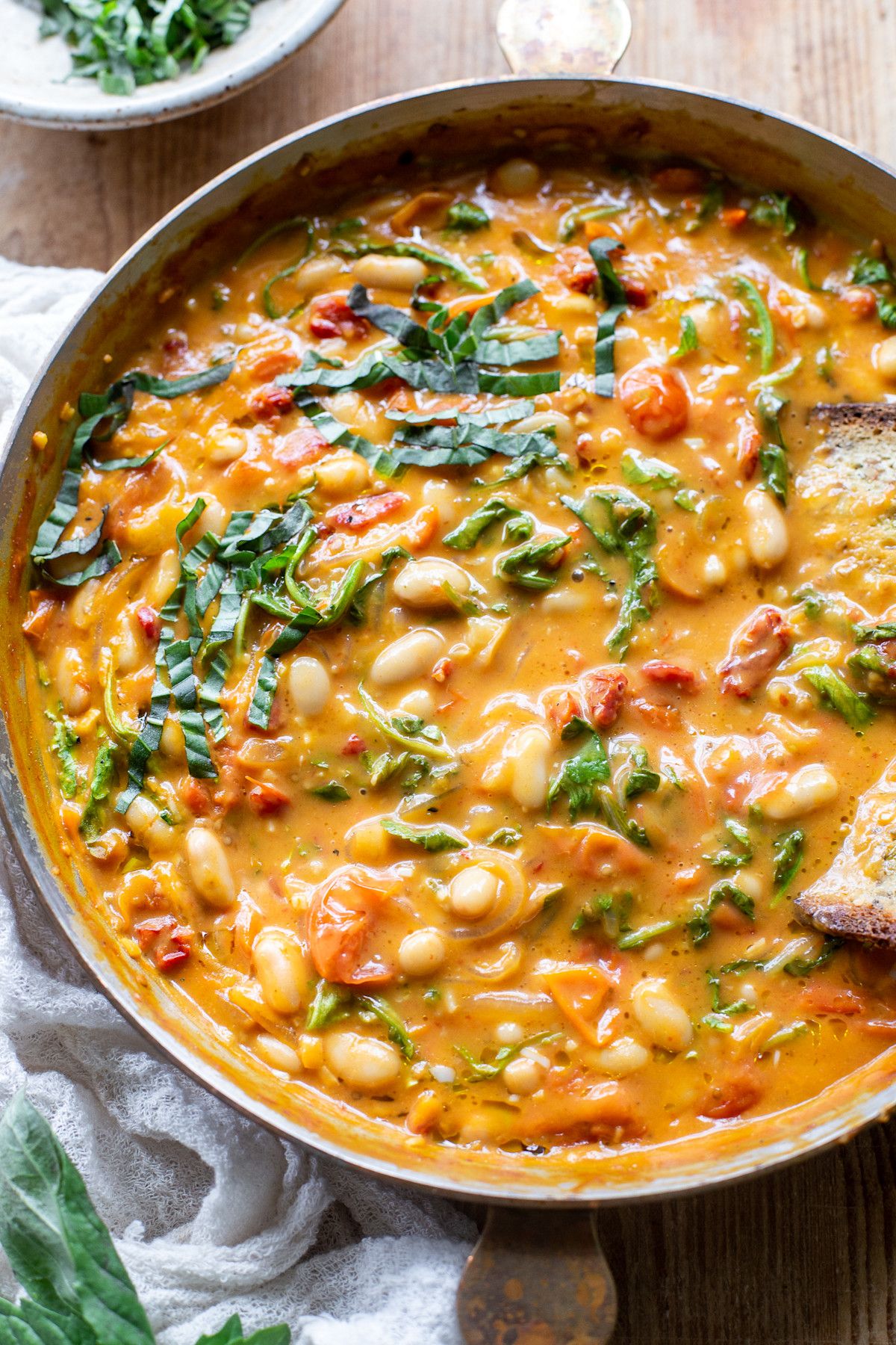 Vegan tomato white bean stew in a pot with a slice of bread.