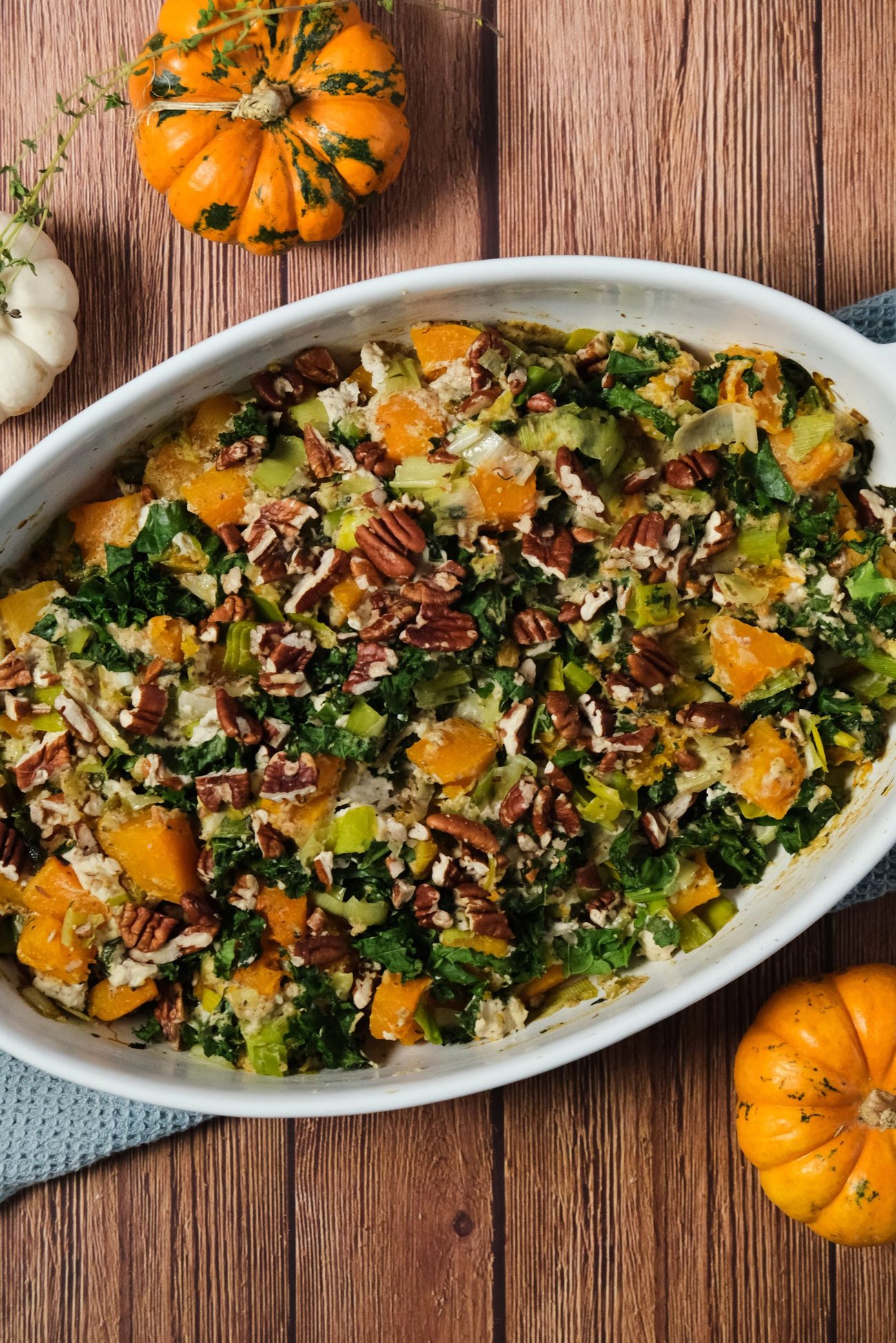 Butternut squash casserole in a casserole dish with small pumpkins nearby