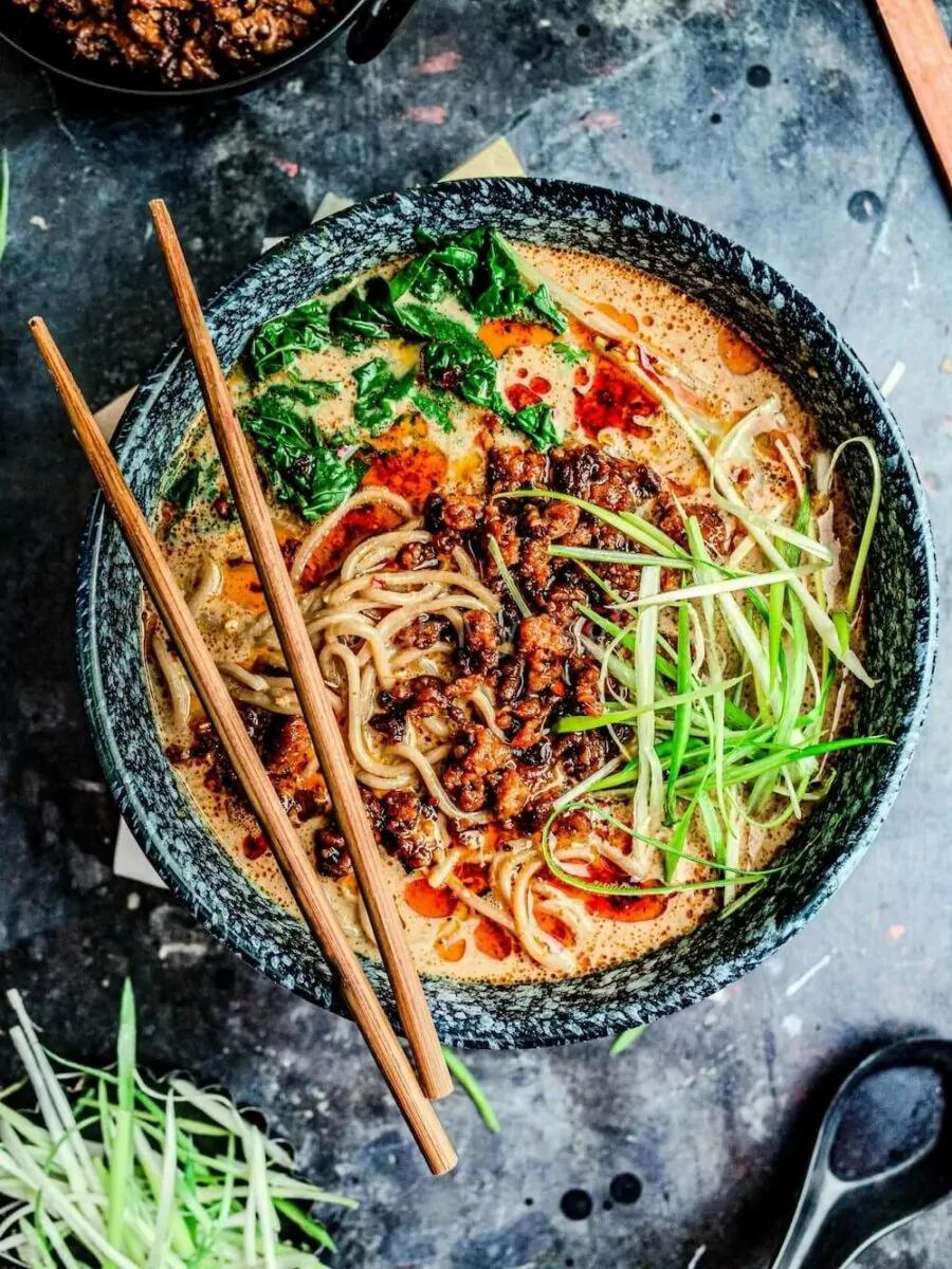 A bowl of vegan tantanmen ramen with chopsticks on top and a soup spoon on the side. 