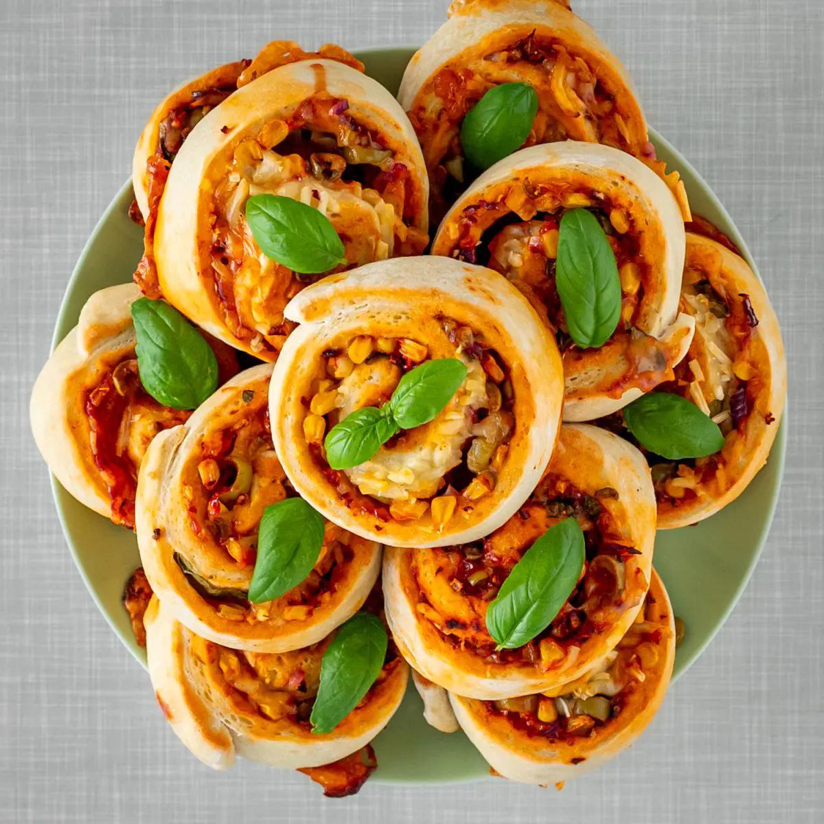 Vegan pizza rolls stacked on a plate, topped with basil leaves. 
