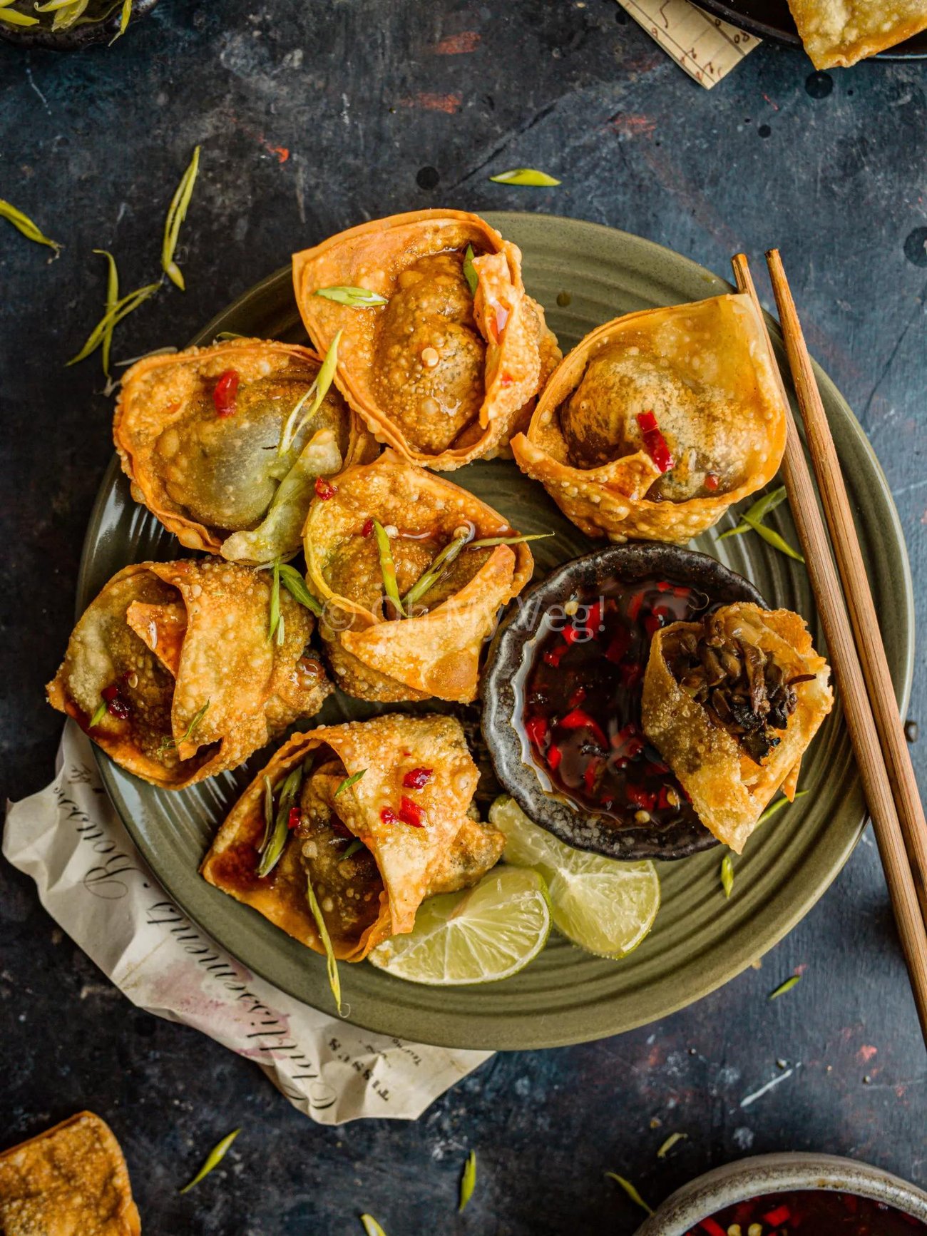 A plate of vegan mushroom wontons with a small bowl of dipping sauce and a pair of chopsticks. 