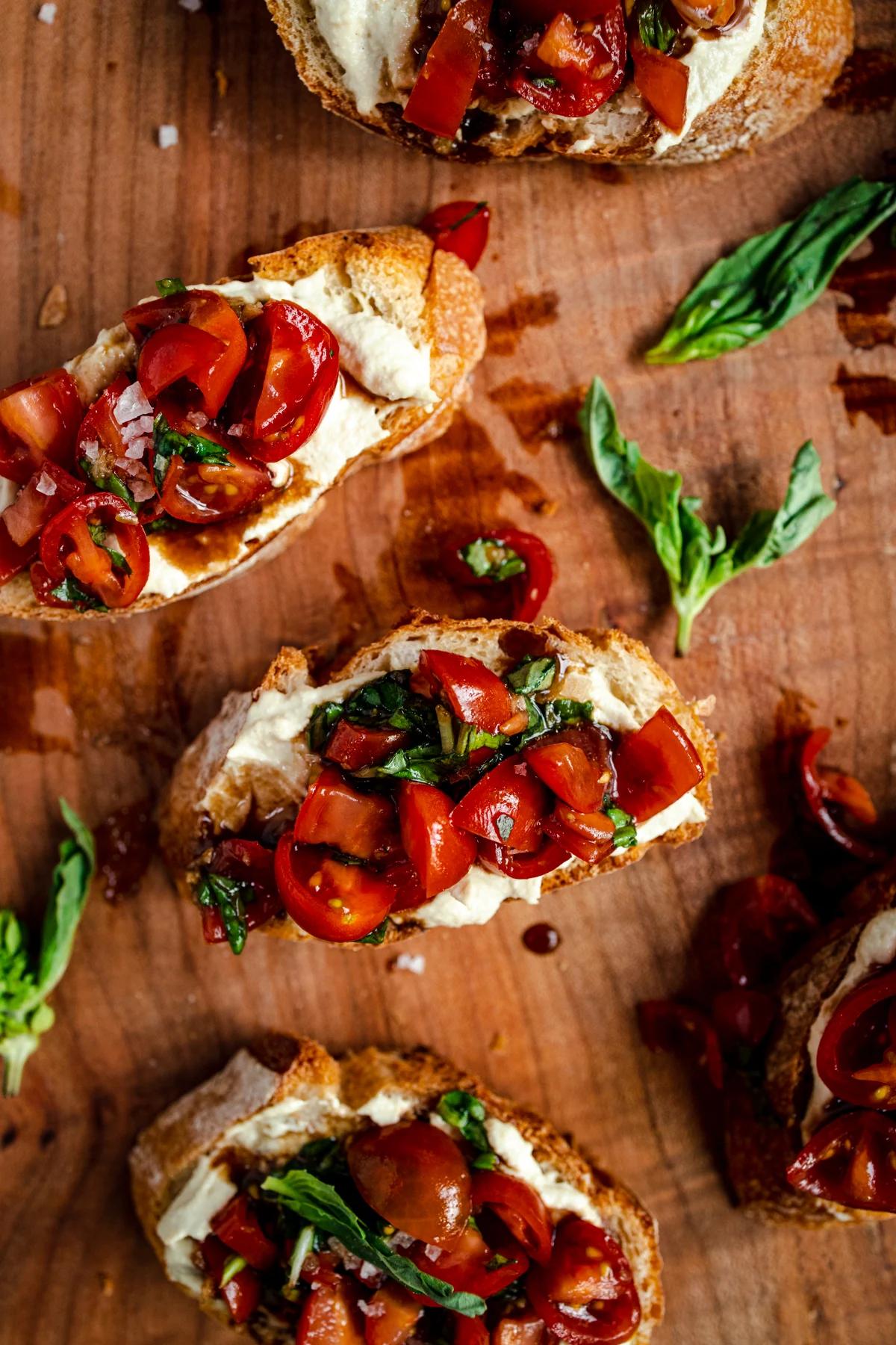 Vegan bruschetta scattered on a wooden surface with chopped herbs. 