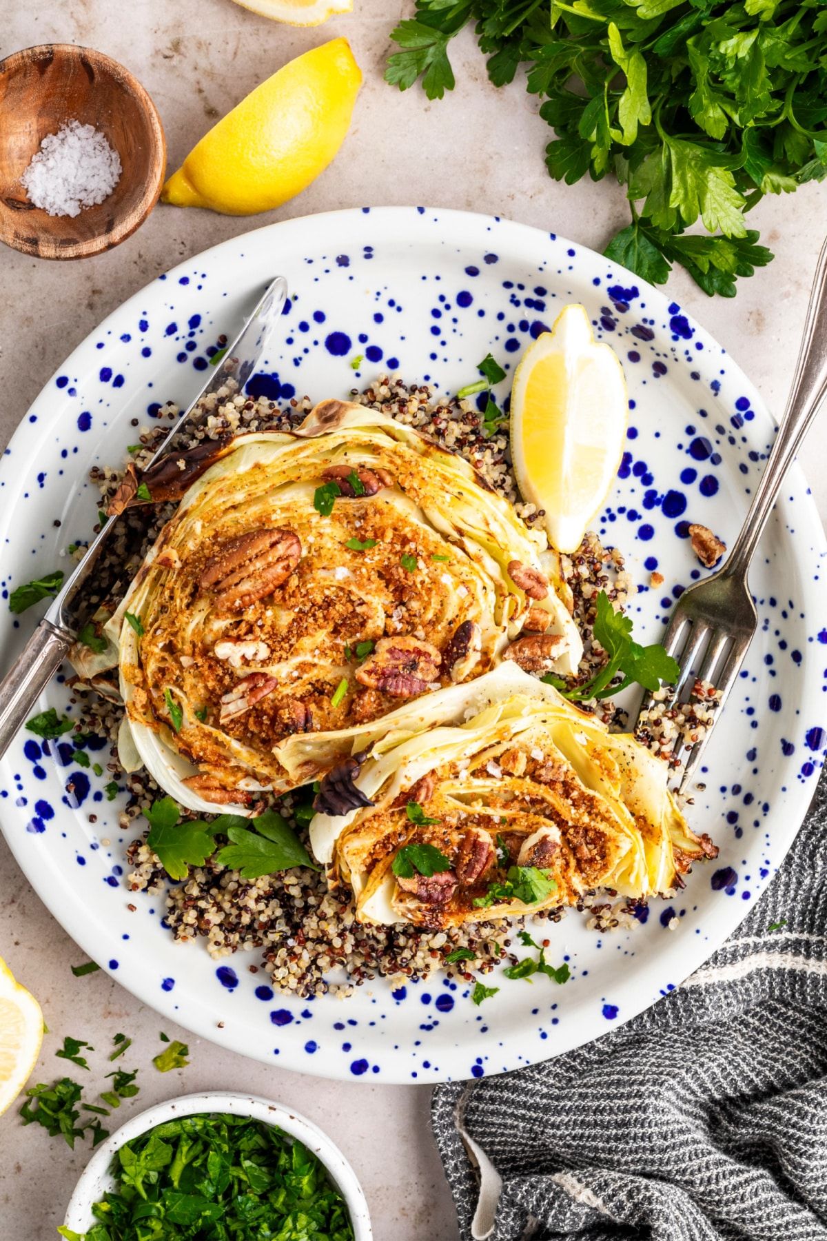 Maple mustard roasted cabbage steaks on a plate with silverware, surrounded by lemon wedges and herbs.