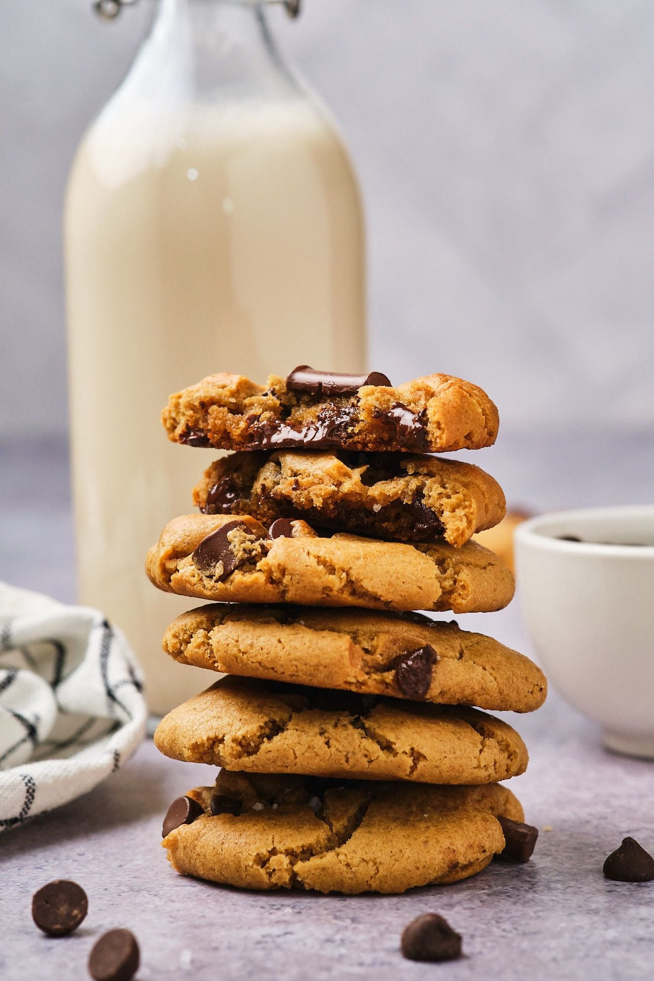 A stack of vegan chocolate chip cookies on a table, with a jug of non-dairy milk in the background.