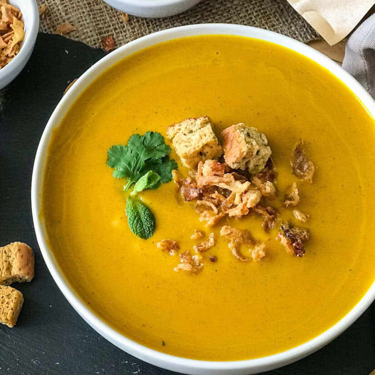 A bowl of sweet potato turmeric soup topped with croutons and herbs. 