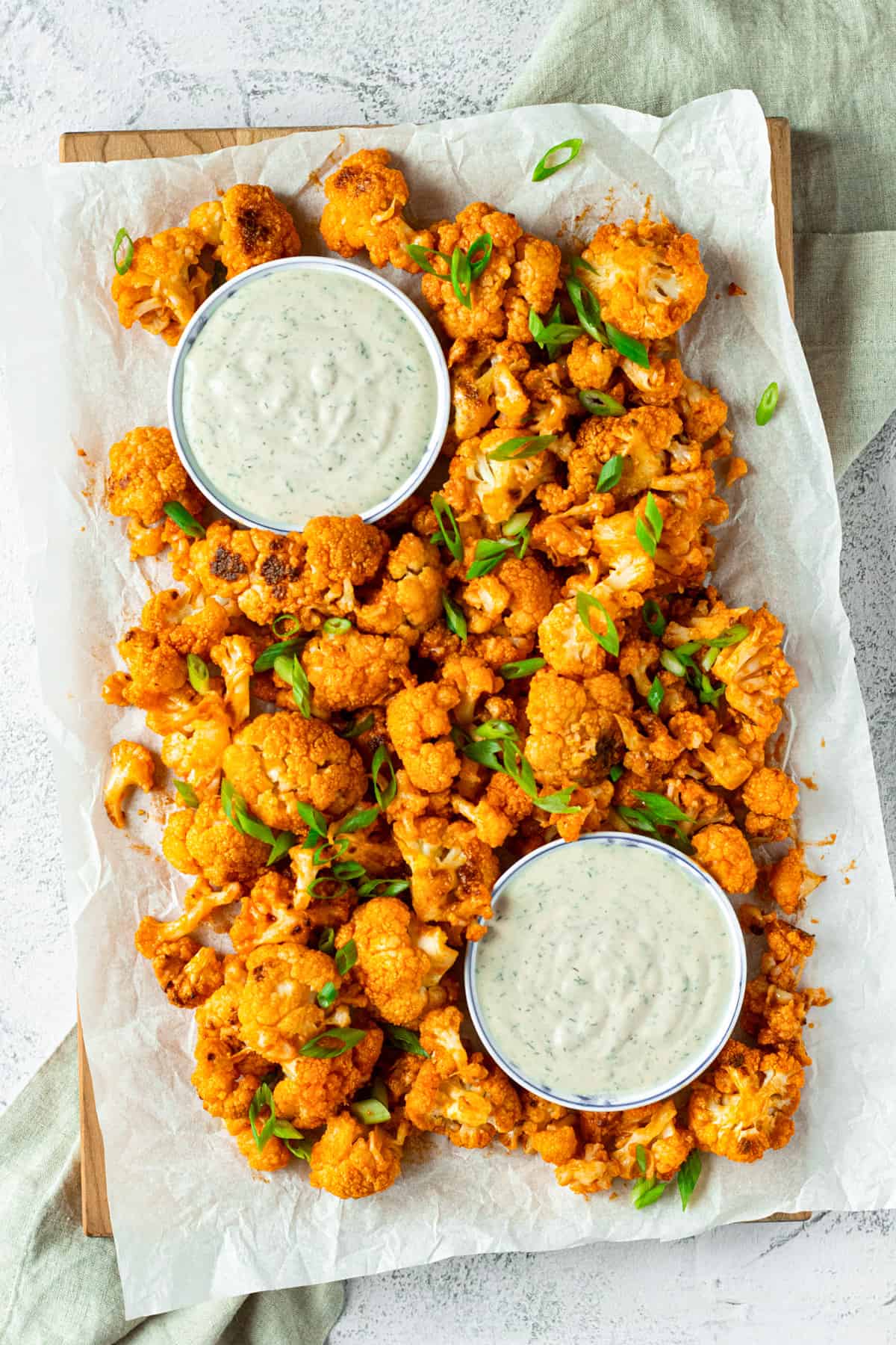 Buffalo cauliflower bites on a large wooden platter with two bowls of tahini ranch dip. 