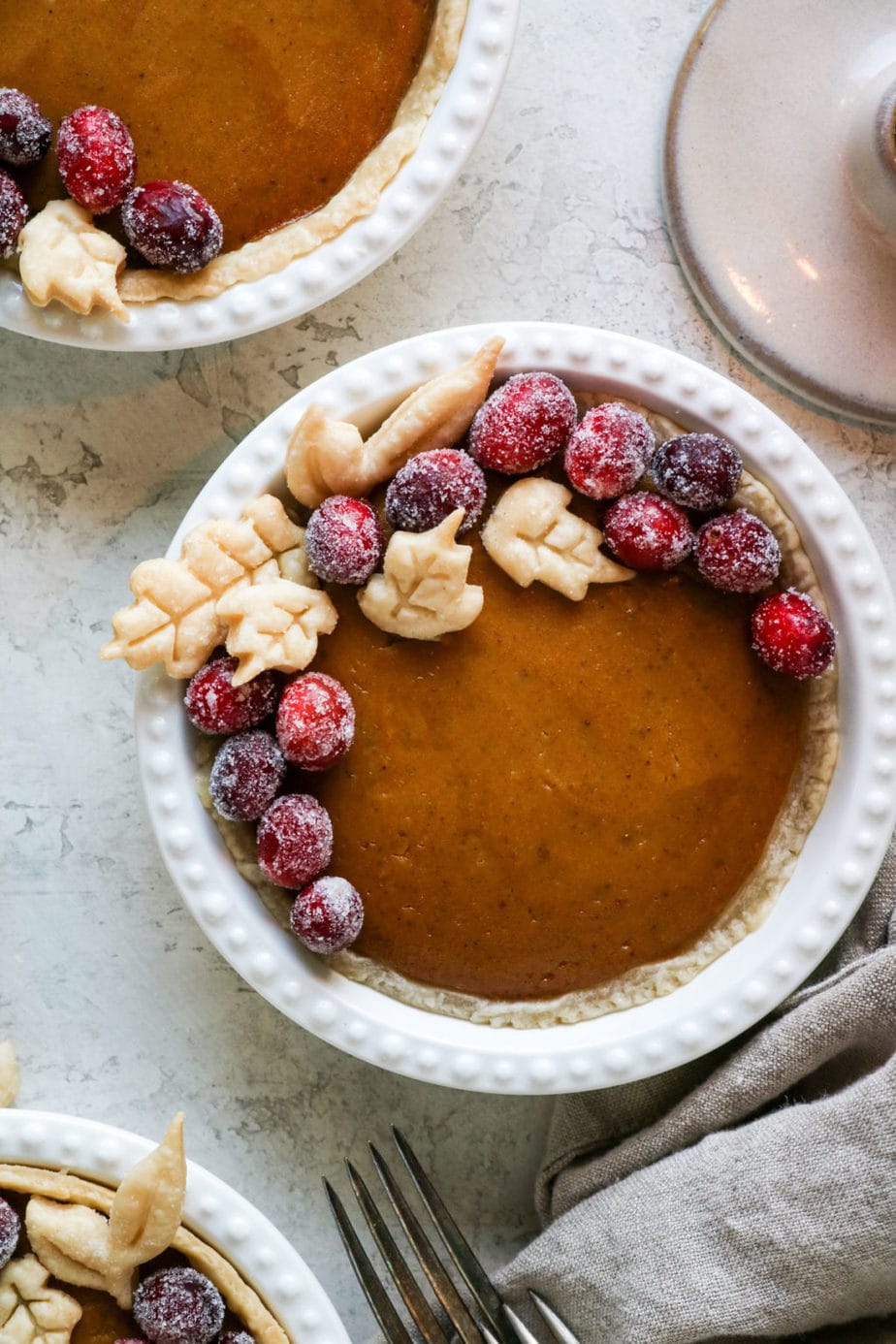 Mini vegan pumpkin pies topped with pie crust leaves and frosted cranberries. 