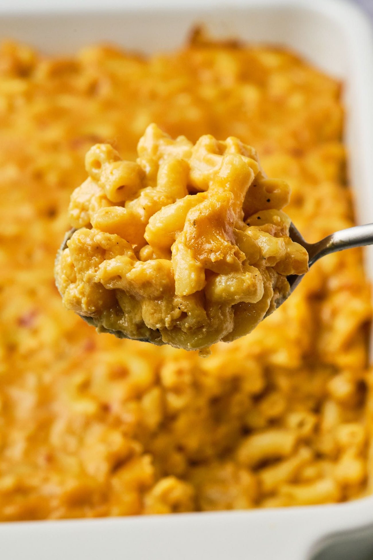 Vegan mac and cheese on a serving spoon in front of a casserole dish of mac and cheese.