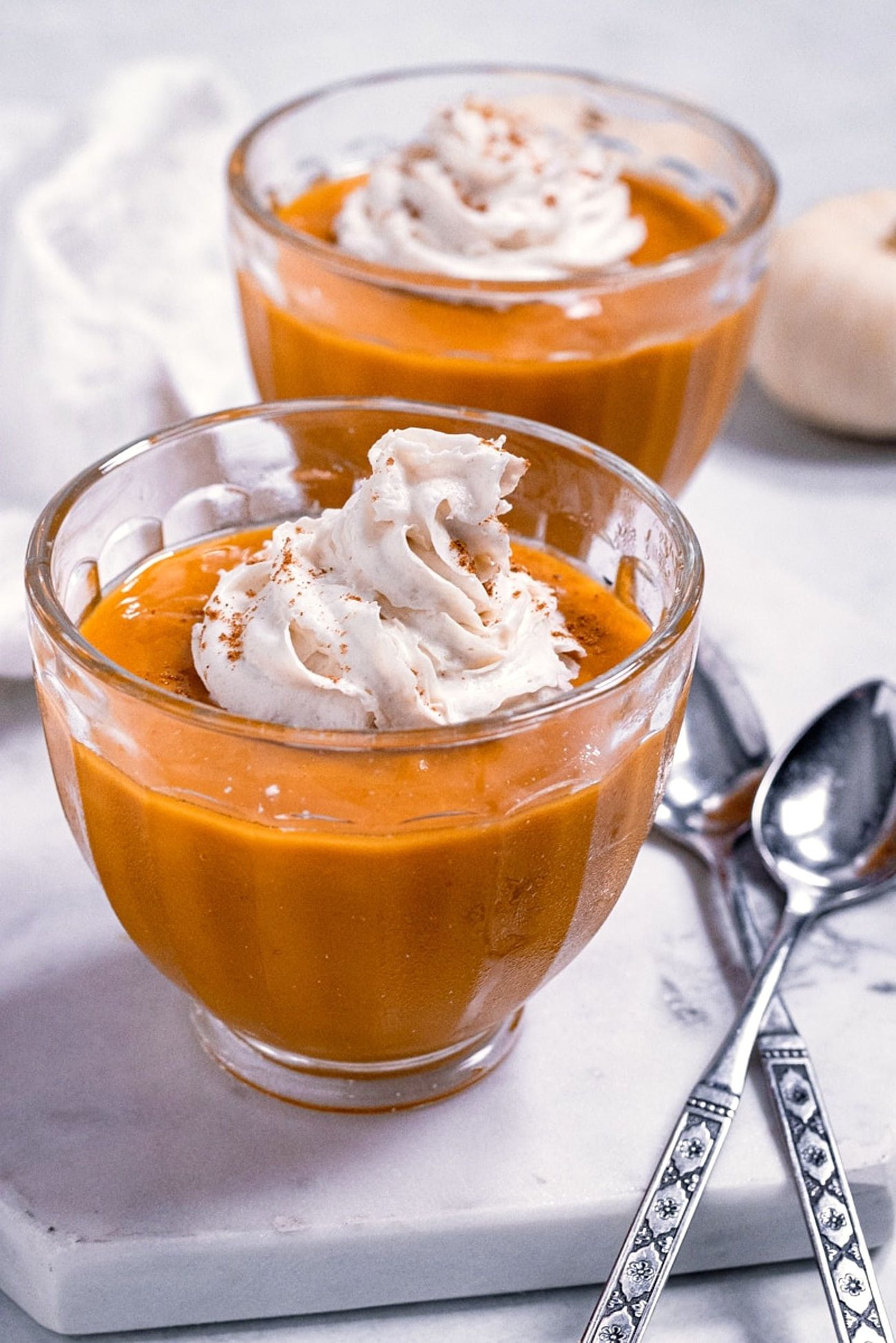 Two bowls of vegan pumpkin custard, topped with vegan whipped cream.