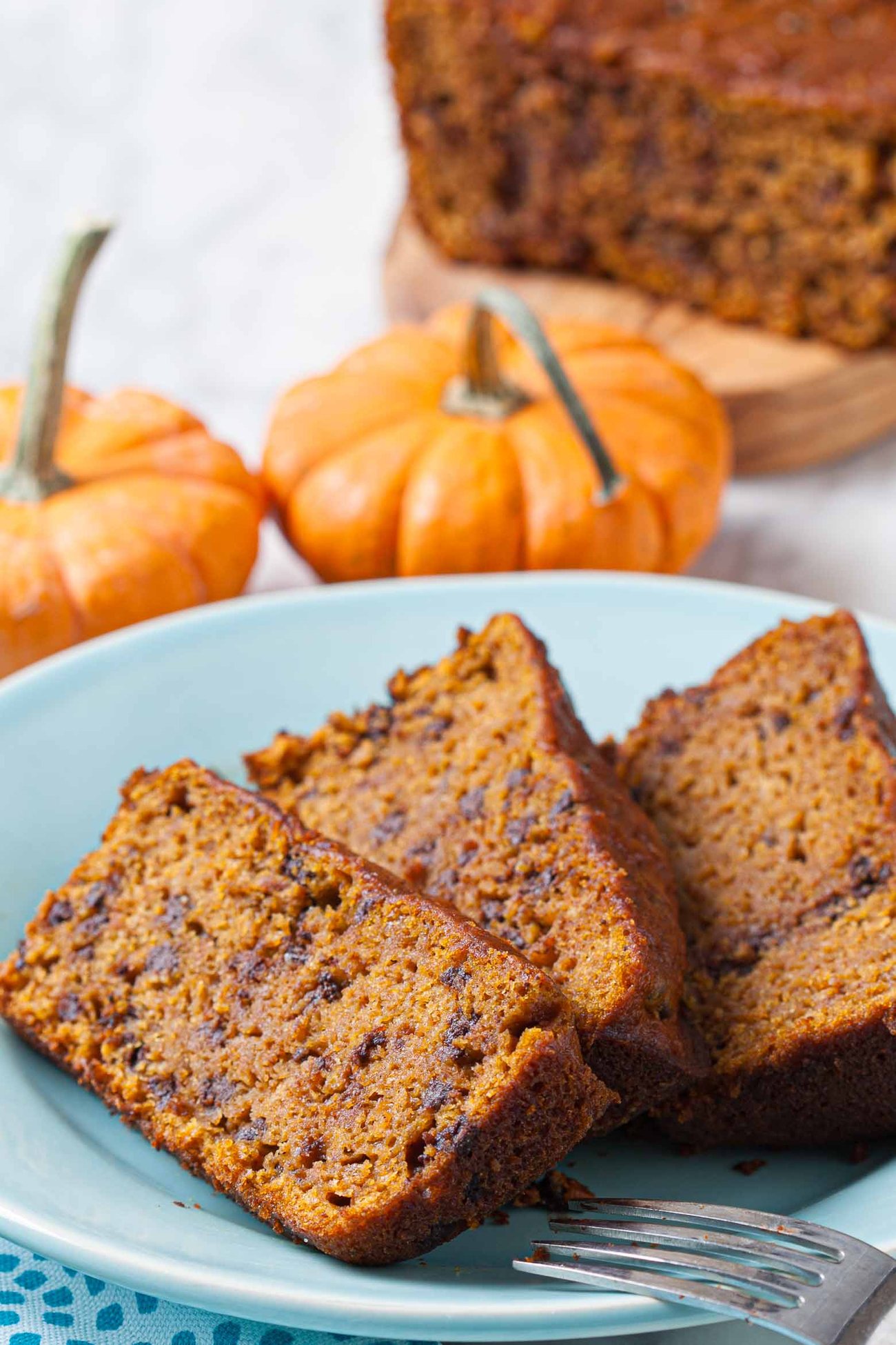 Vegan pumpkin bread slices on a plate with the loaf of bread in the background. 