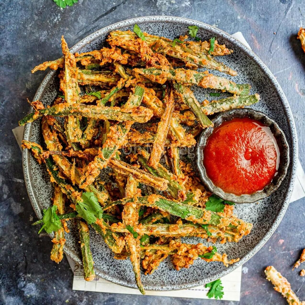 Okra fries on a plate with a ramekin of ketchup. 