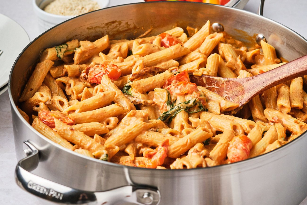 Creamy vegan tomato pasta in a large skillet with a wooden spoon.