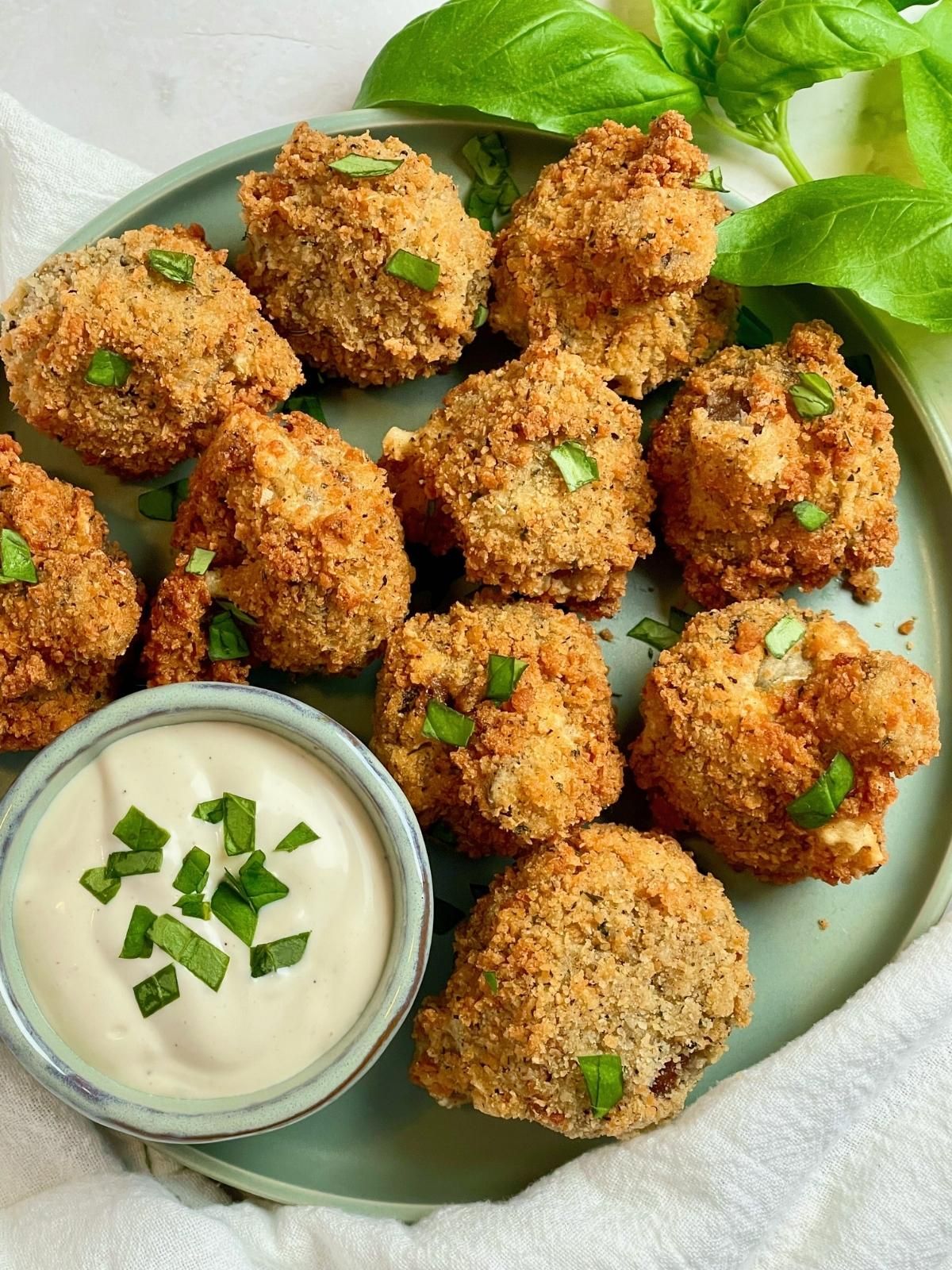 Vegan breaded mushrooms on a plate with basil and a bowl of dipping sauce.