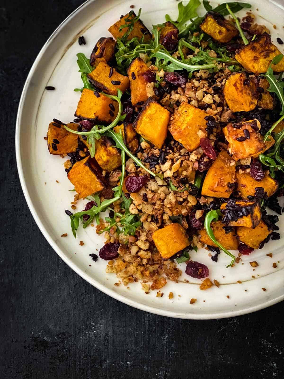 Arugula salad with butternut squash and cranberries on a plate.