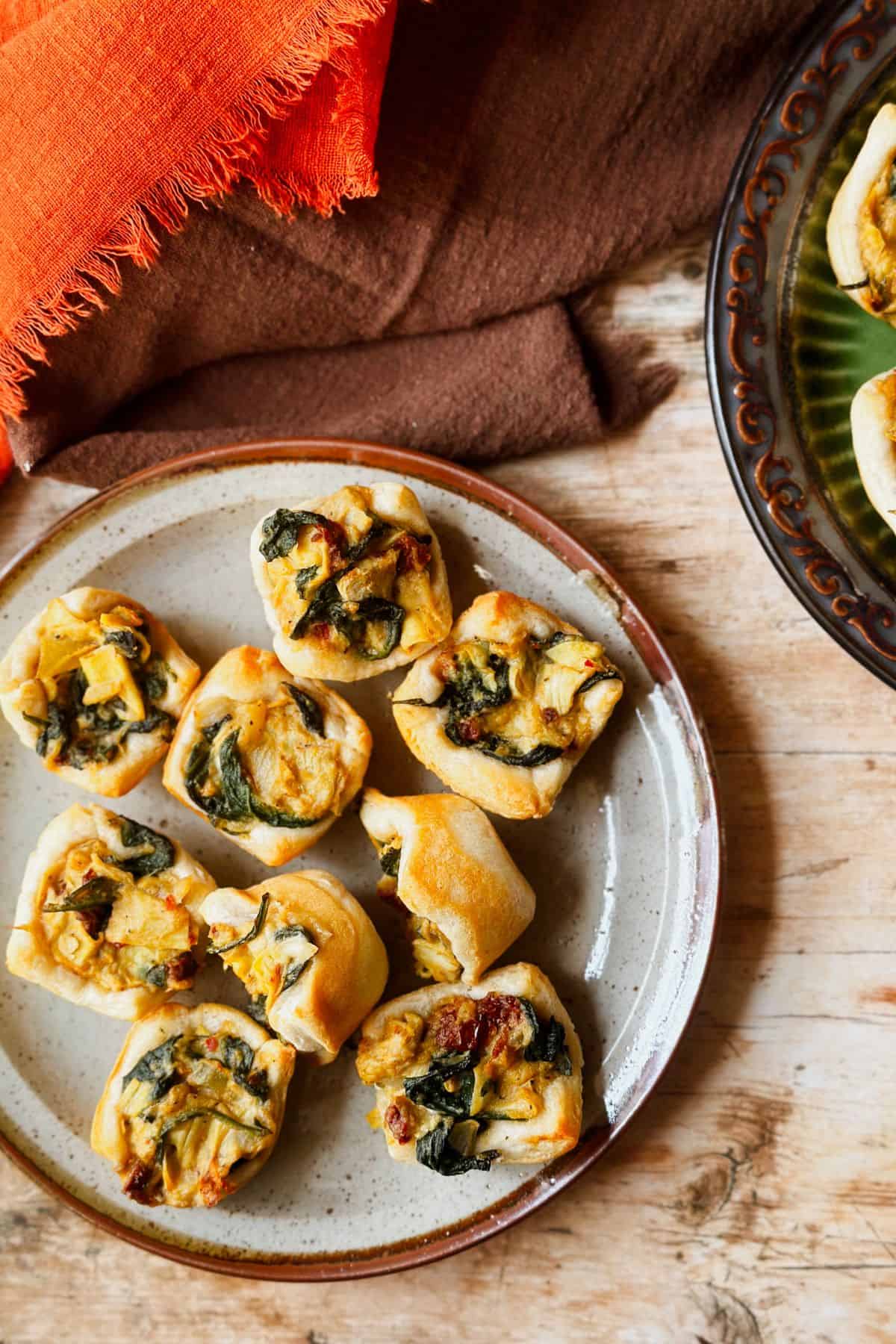 Vegan spinach, artichoke, and sun-dried tomato cups on a plate on a table next to linens.
