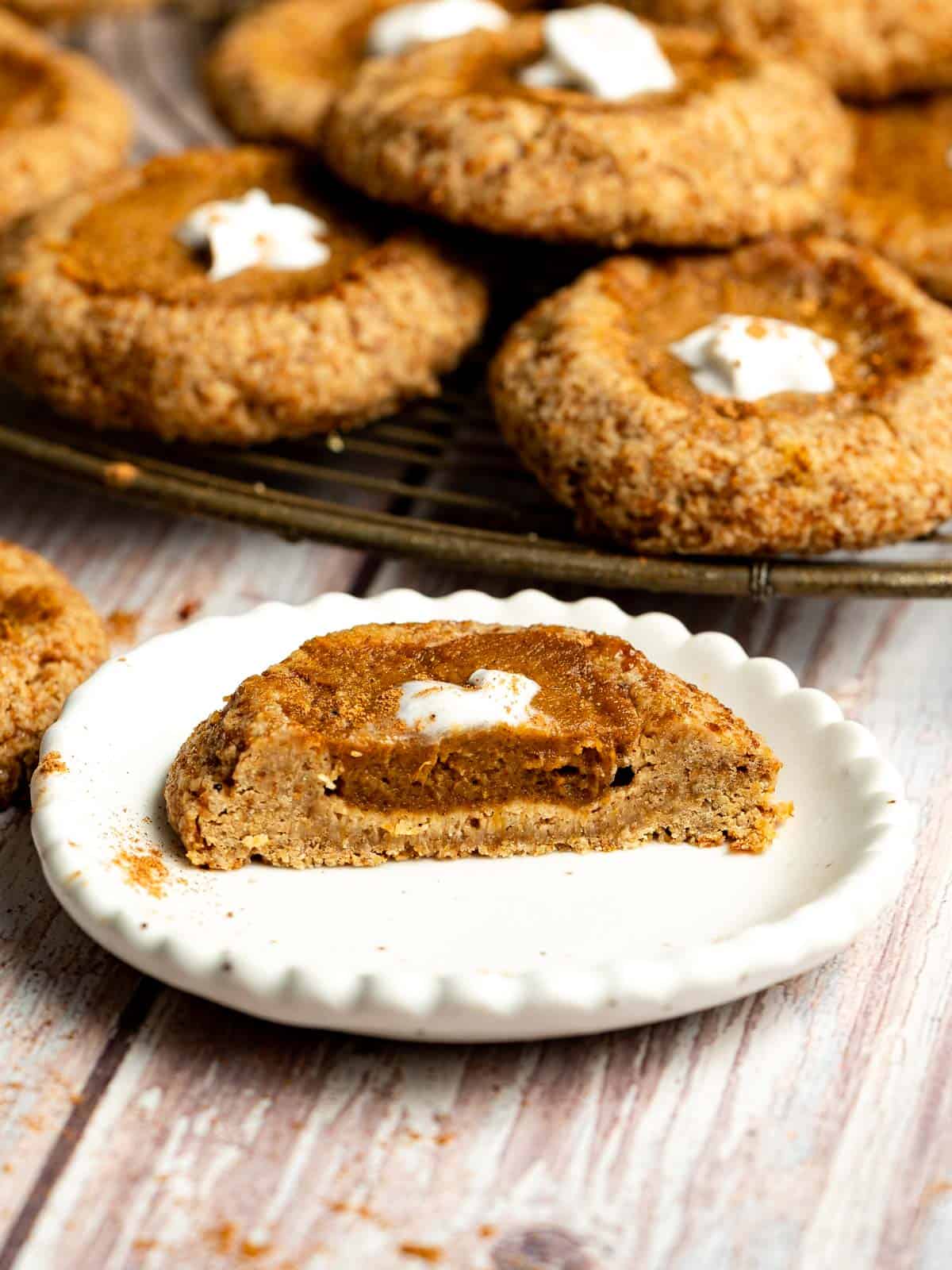 A mini pumpkin pie sugar cookie on a small plate, cut in half to show its filling, with more cookies in the background.