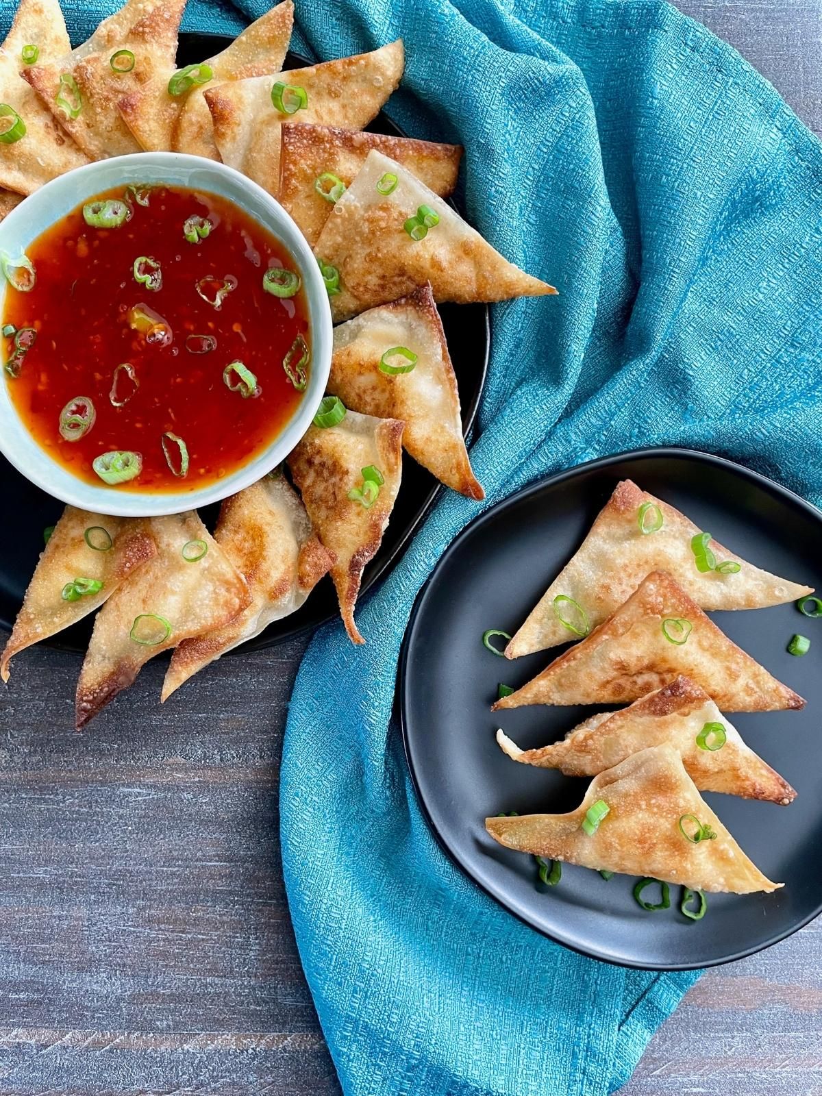 Vegan cream cheese wontons on a platter with sweet and sour dipping sauce, with a small appetizer plate to its side with four wontons. 