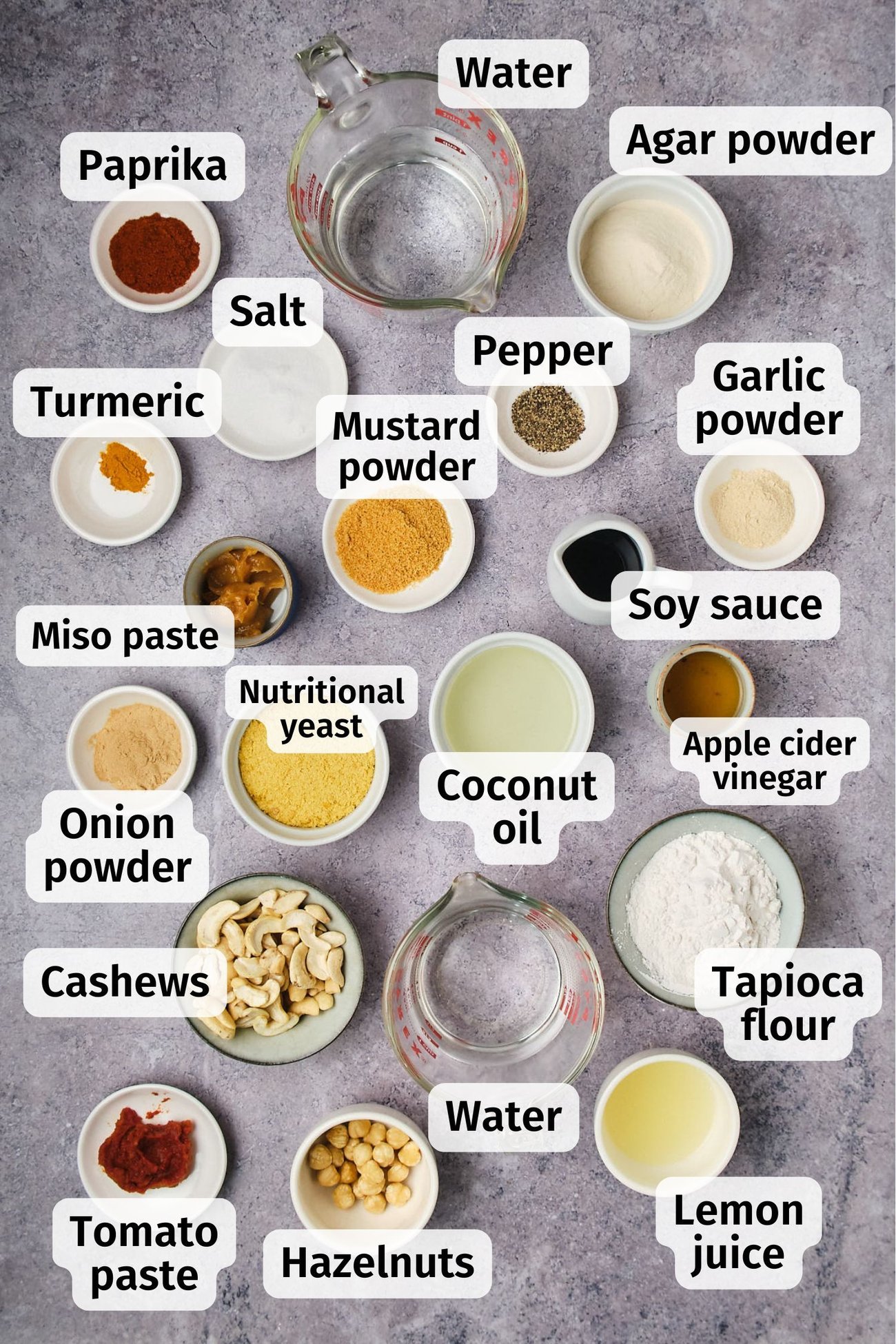 The ingredients for vegan cheddar-Gruyère cheese in individual dishes, labeled, on a table.