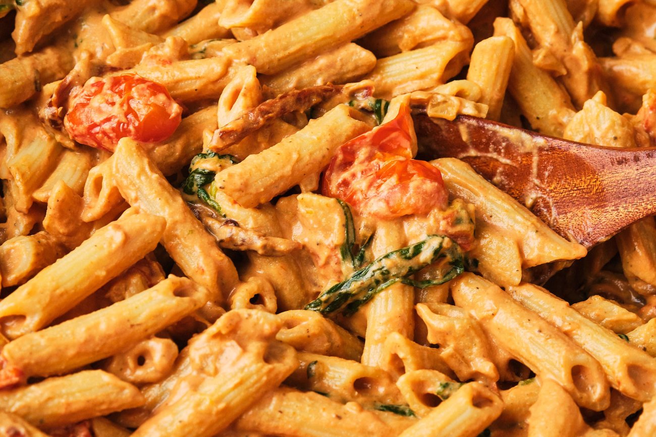 A close-up image of creamy vegan tomato pasta with a wooden spoon.