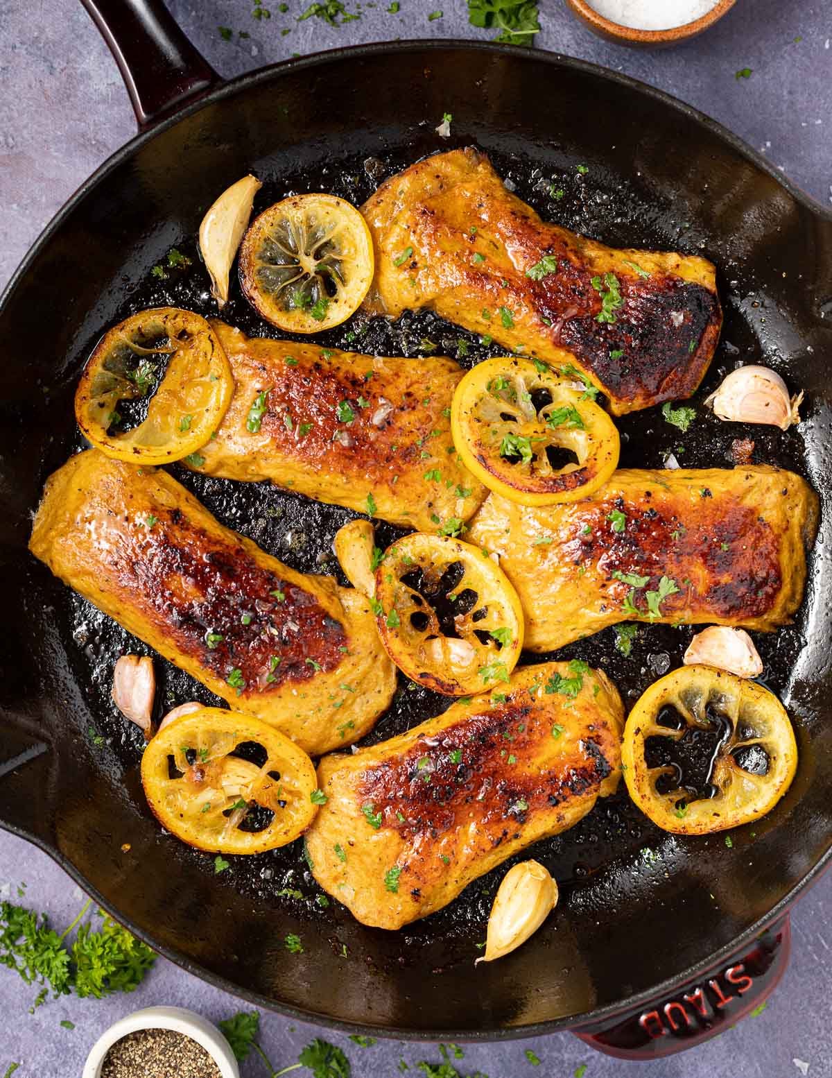 Vegan chicken breasts in a pan with lemon slices and garlic cloves.