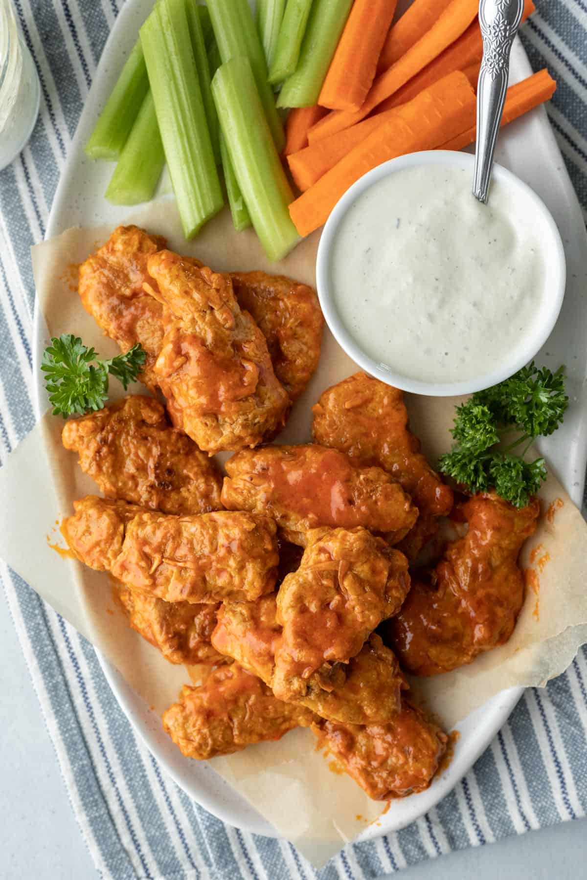 Vegan buffalo wings on a platter with a bowl of dipping sauce and carrot and celery sticks.