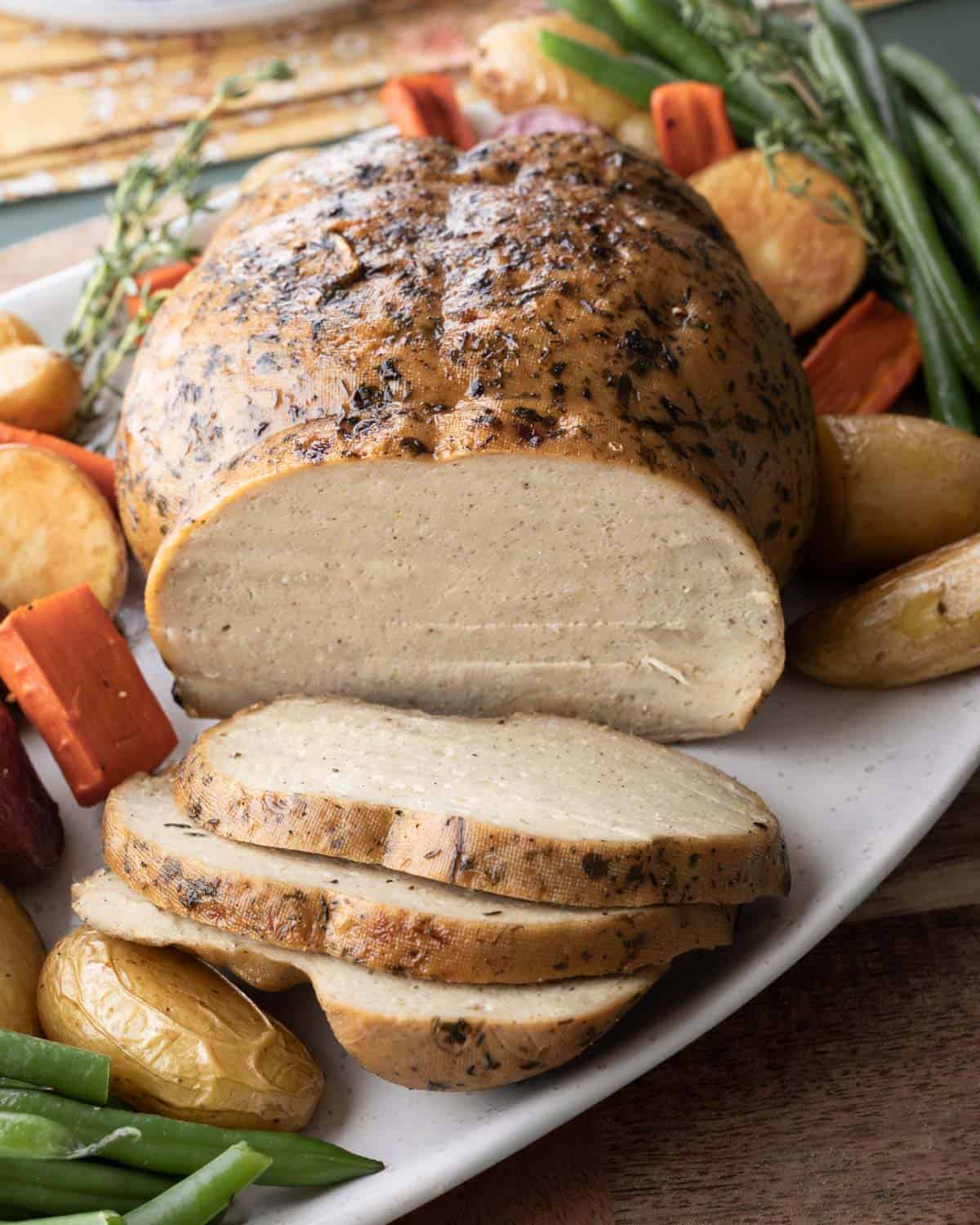 Homemade vegan turkey, sliced, on a platter with vegetables. 