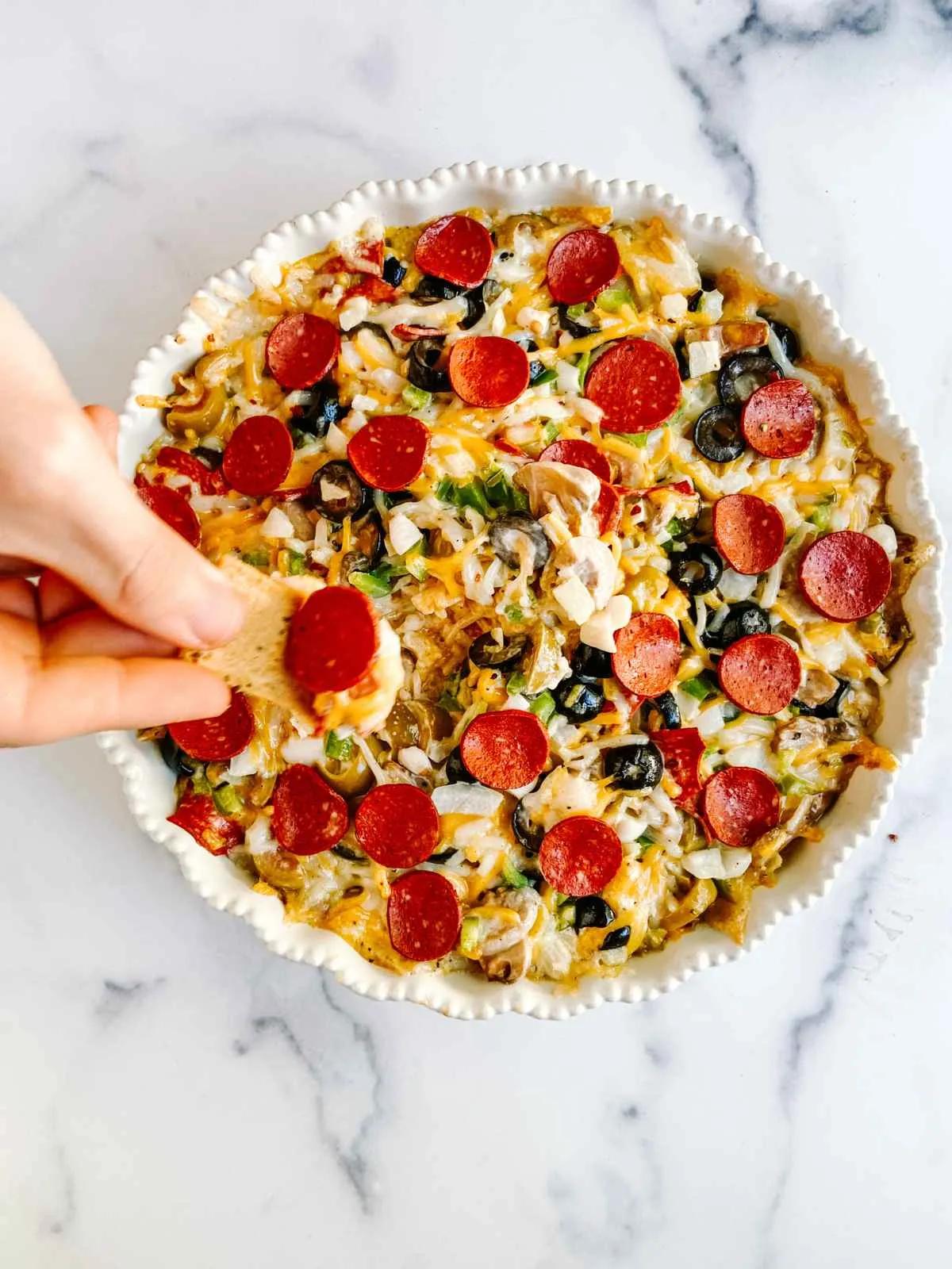 A hand dipping a cracker into a large bowl of vegan pizza dip. 