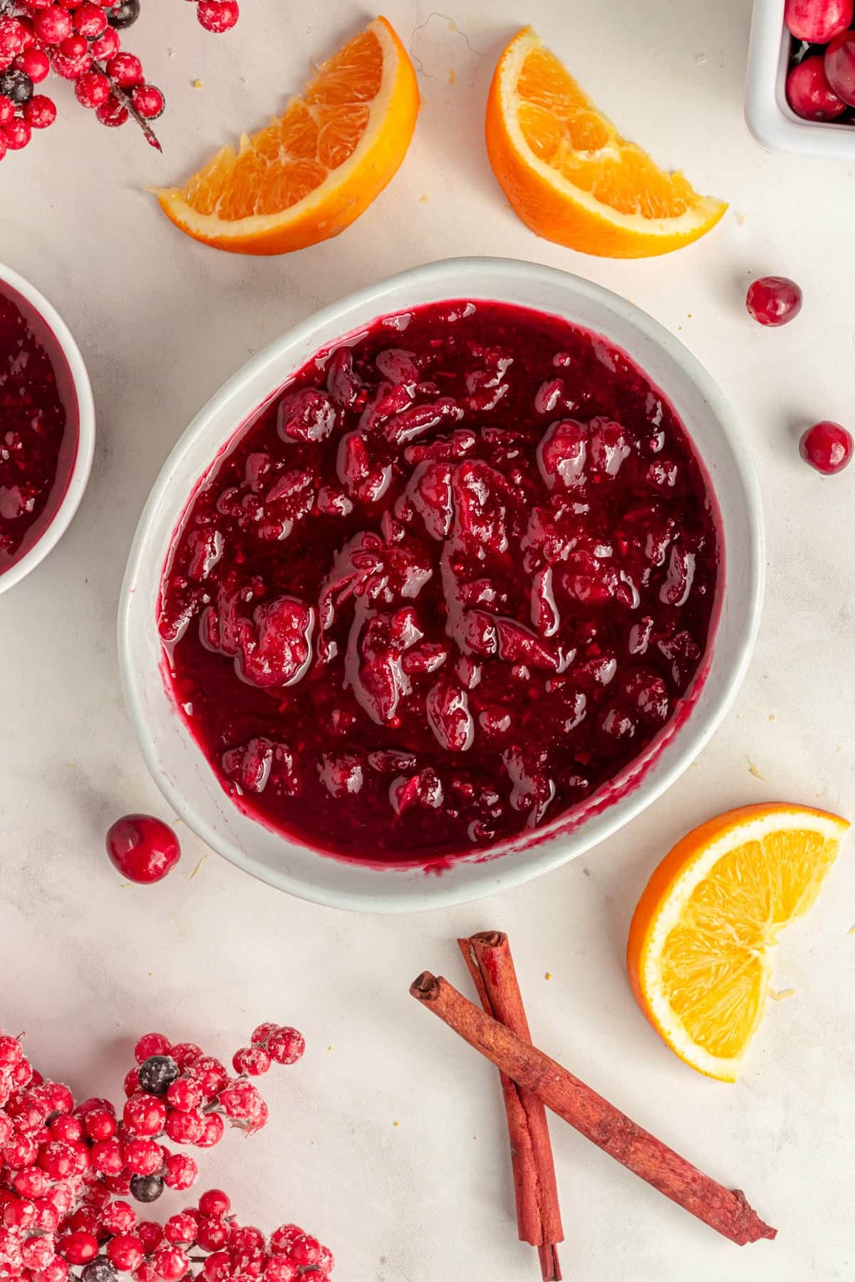 Vegan cranberry sauce in a bowl, surrounded by cinnamon sticks, orange slices, and cranberries.