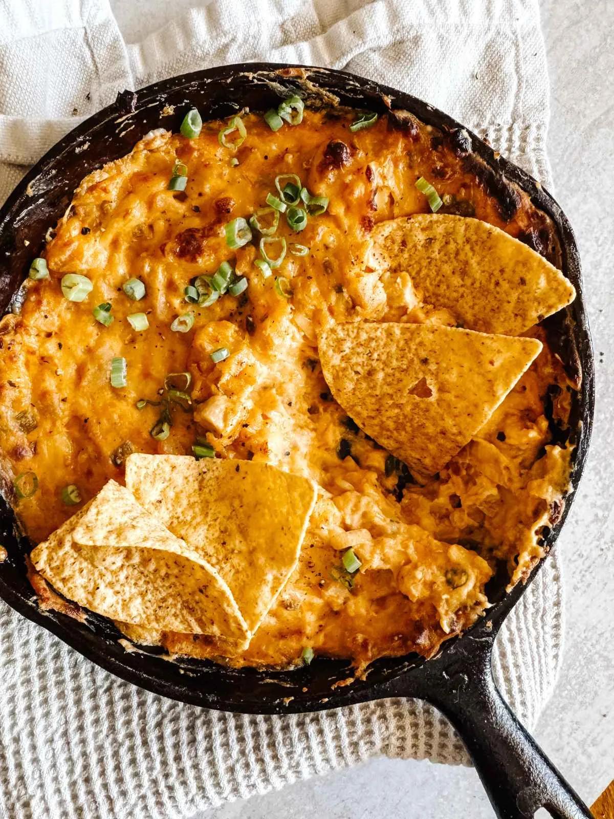 Vegan buffalo chicken dip with tortilla chips in a cast-iron pan.