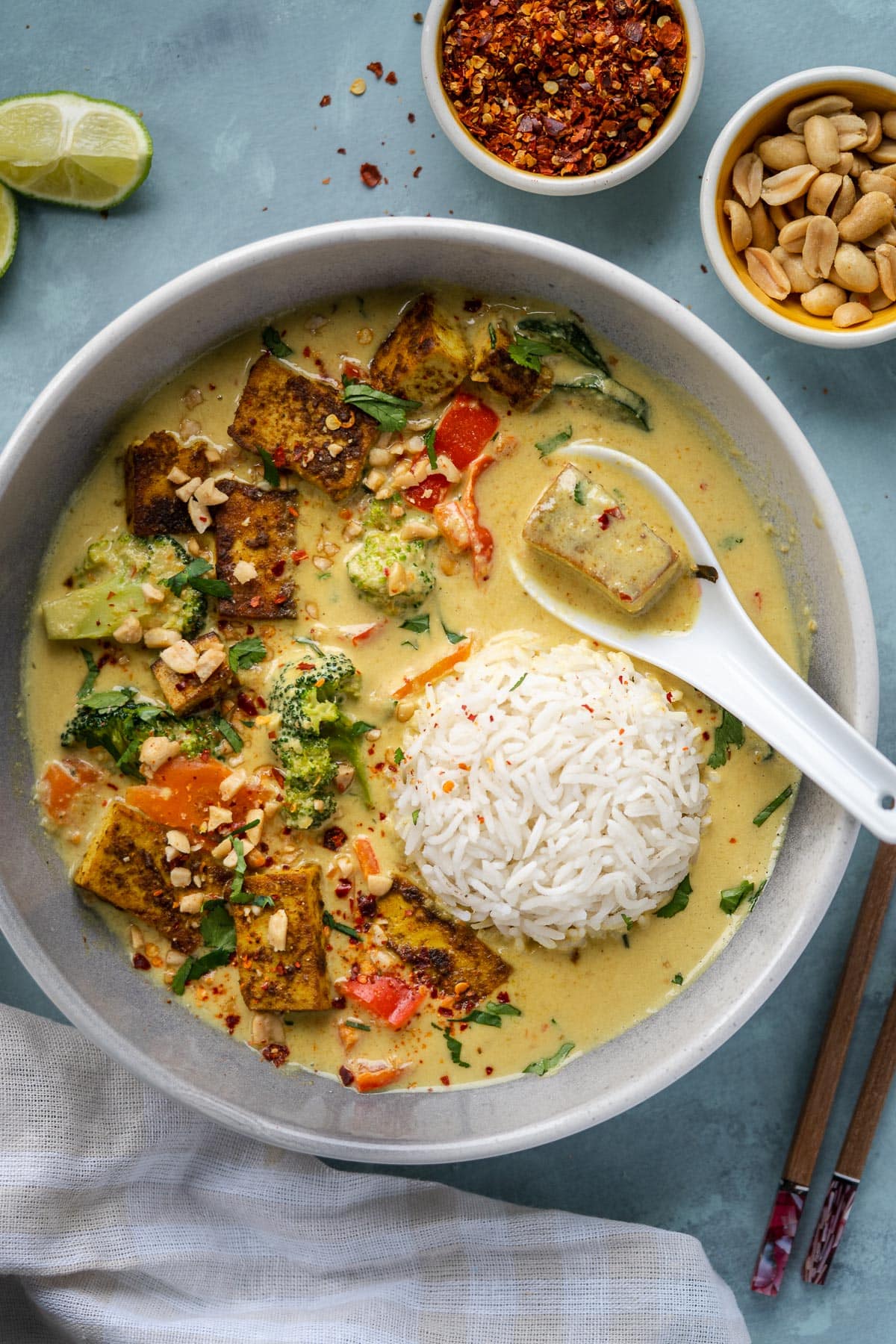 Vegan Thai peanut curry in a bowl next to small pinch bowls of red pepper flakes and peanuts. 