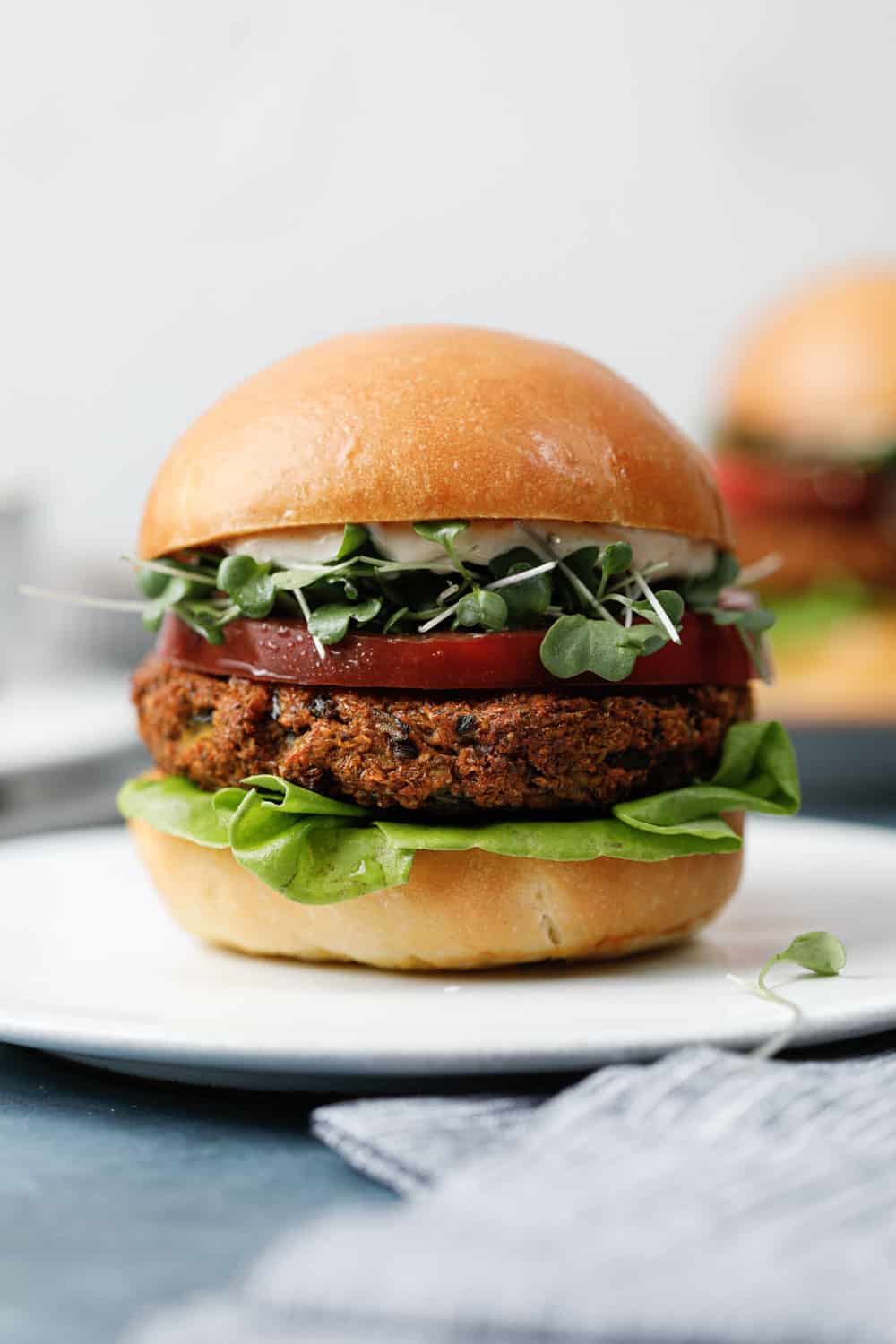 A side view of an edamame and mushroom burger on a plate, topped with lettuce and tomato.