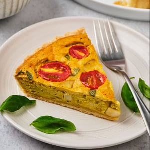 A slice of vegan quiche on a plate with a fork and basil leaves. 