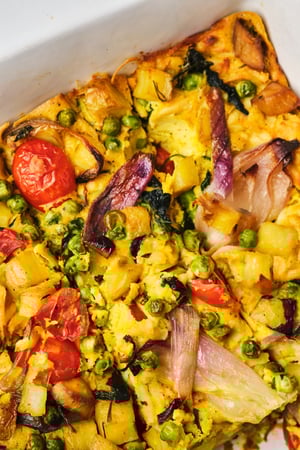 A top-down view of a veggie breakfast casserole in a casserole dish, sliced.