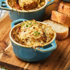 Vegan French Onion Soup in small bowls on a wooden platter next to a spoon and baguette slices. 
