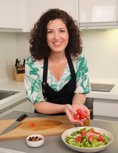 Steph in the kitchen preparing a salad, holding chopped tomatoes in her hands.