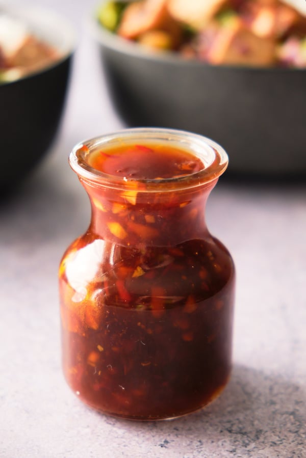 A jar of sweet chili vegan stir-fry sauce with bowls of tofu stir-fry in the background